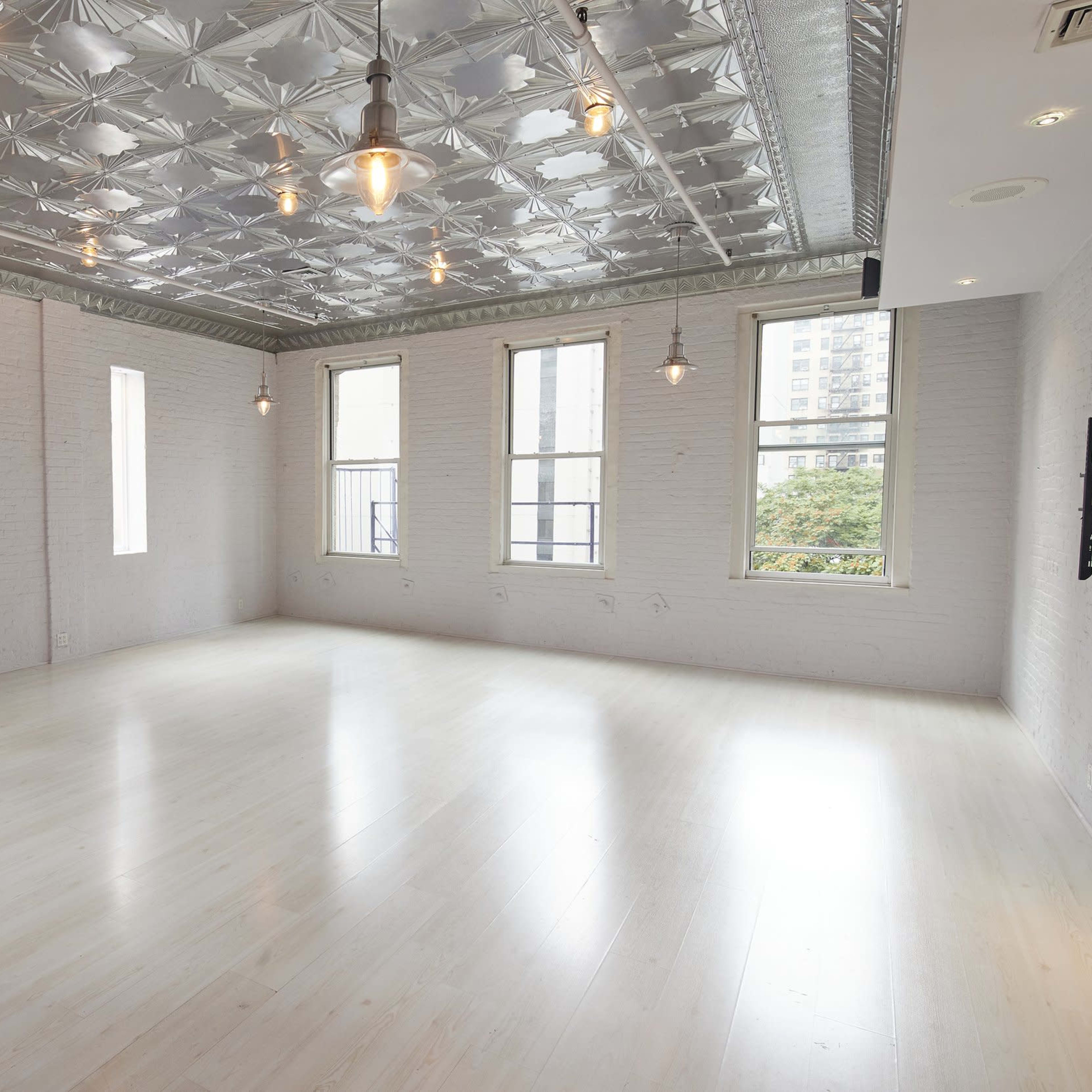 A bright, open room features white brick walls, a silver tin ceiling, and large windows.