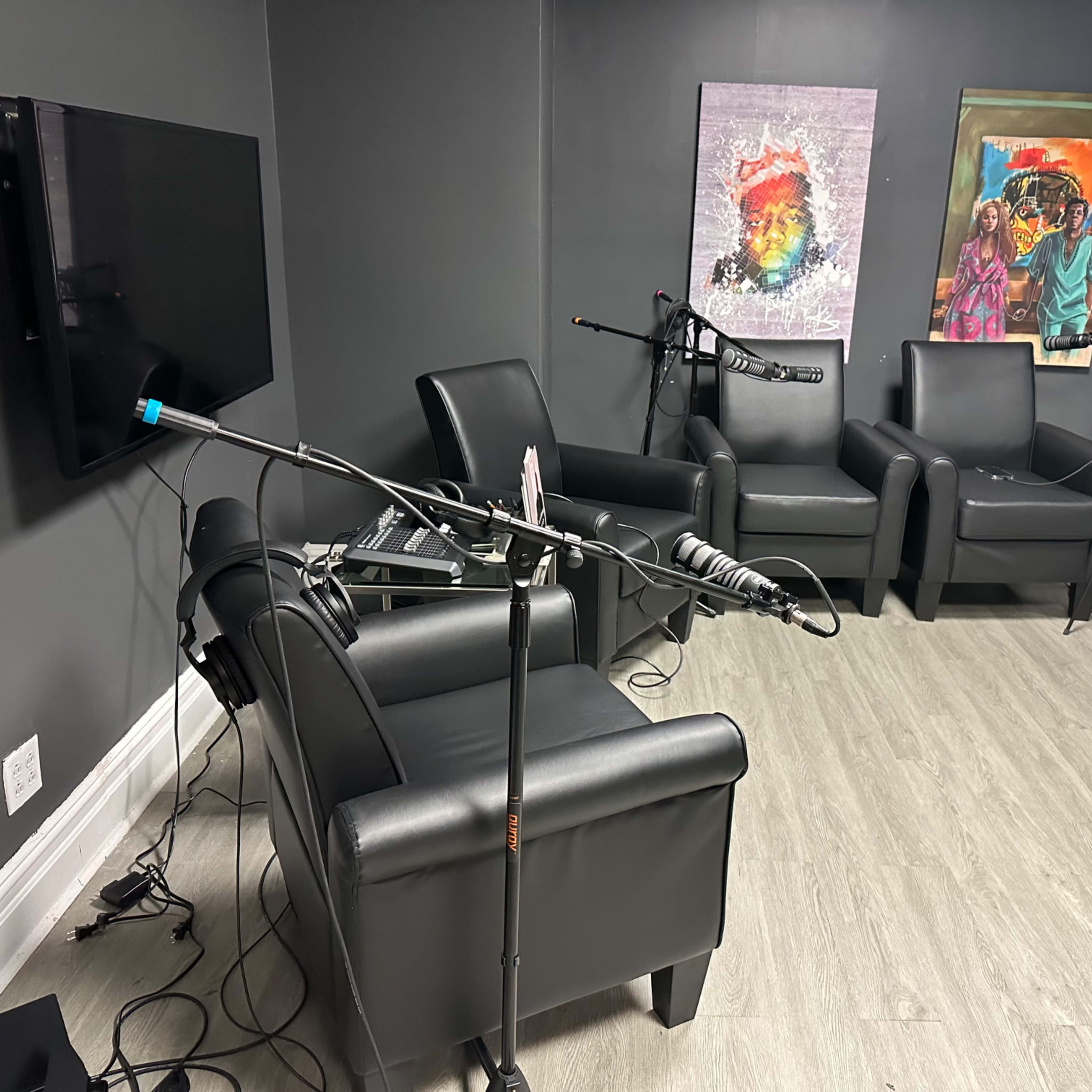 A recording studio setup with black leather chairs, microphones on stands, and colorful artwork on the walls.