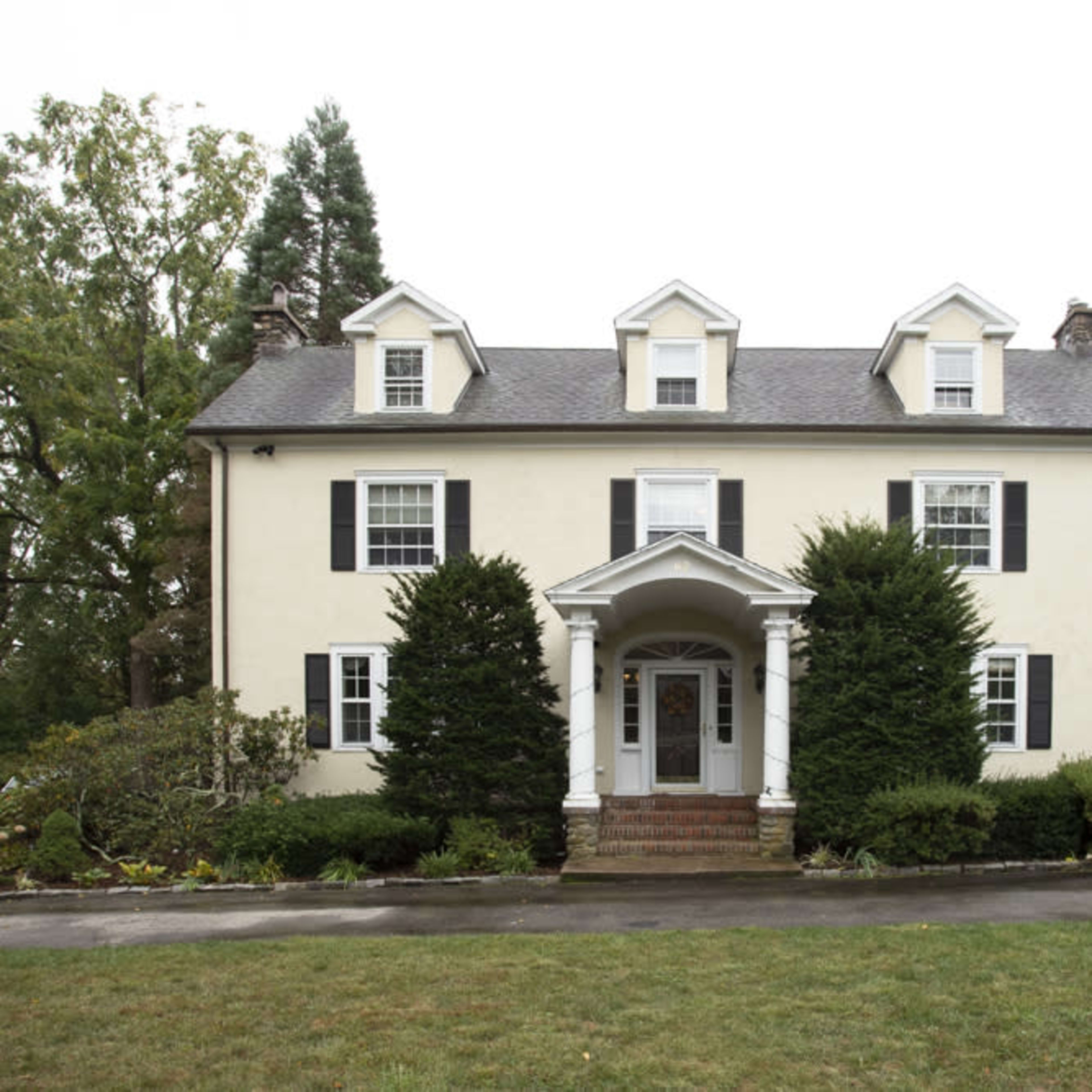 A two-story, colonial-style house with a symmetrical facade, featuring white siding, black shutters, and a front porch supported by columns.