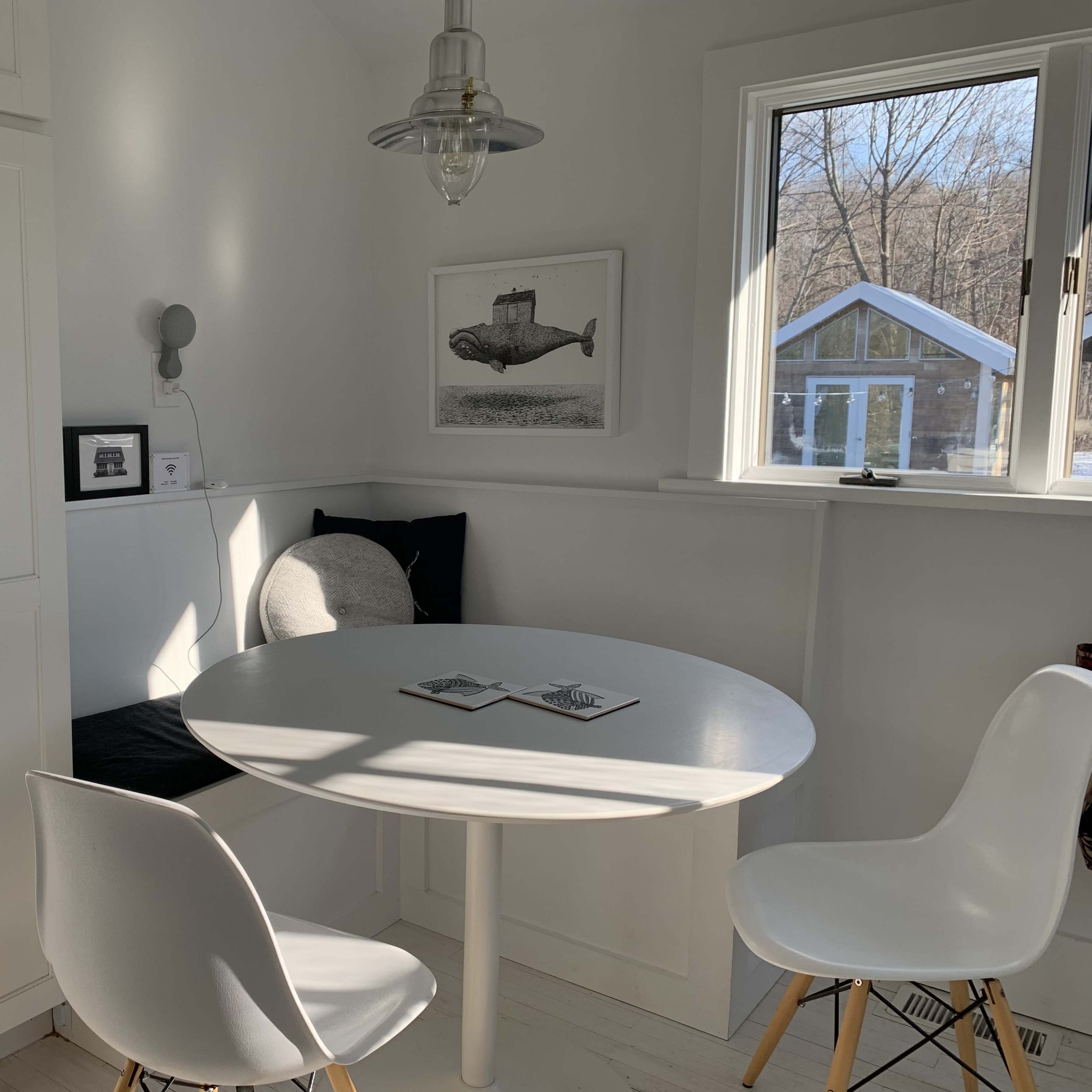 A small dining area features a round white table surrounded by two chairs, with a large window providing natural light.