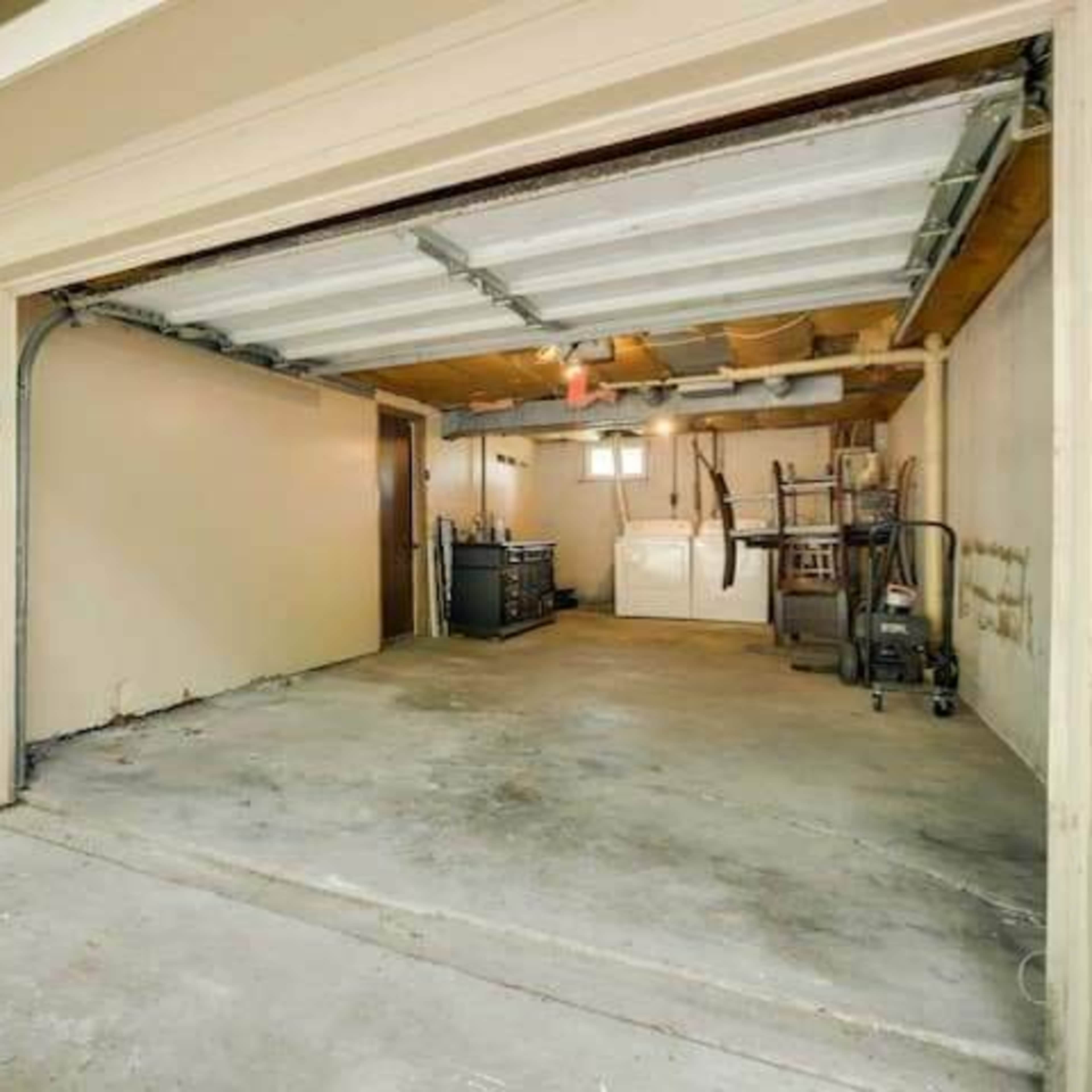 A garage with an open door, featuring a concrete floor, a few appliances, and walls painted in a light color.