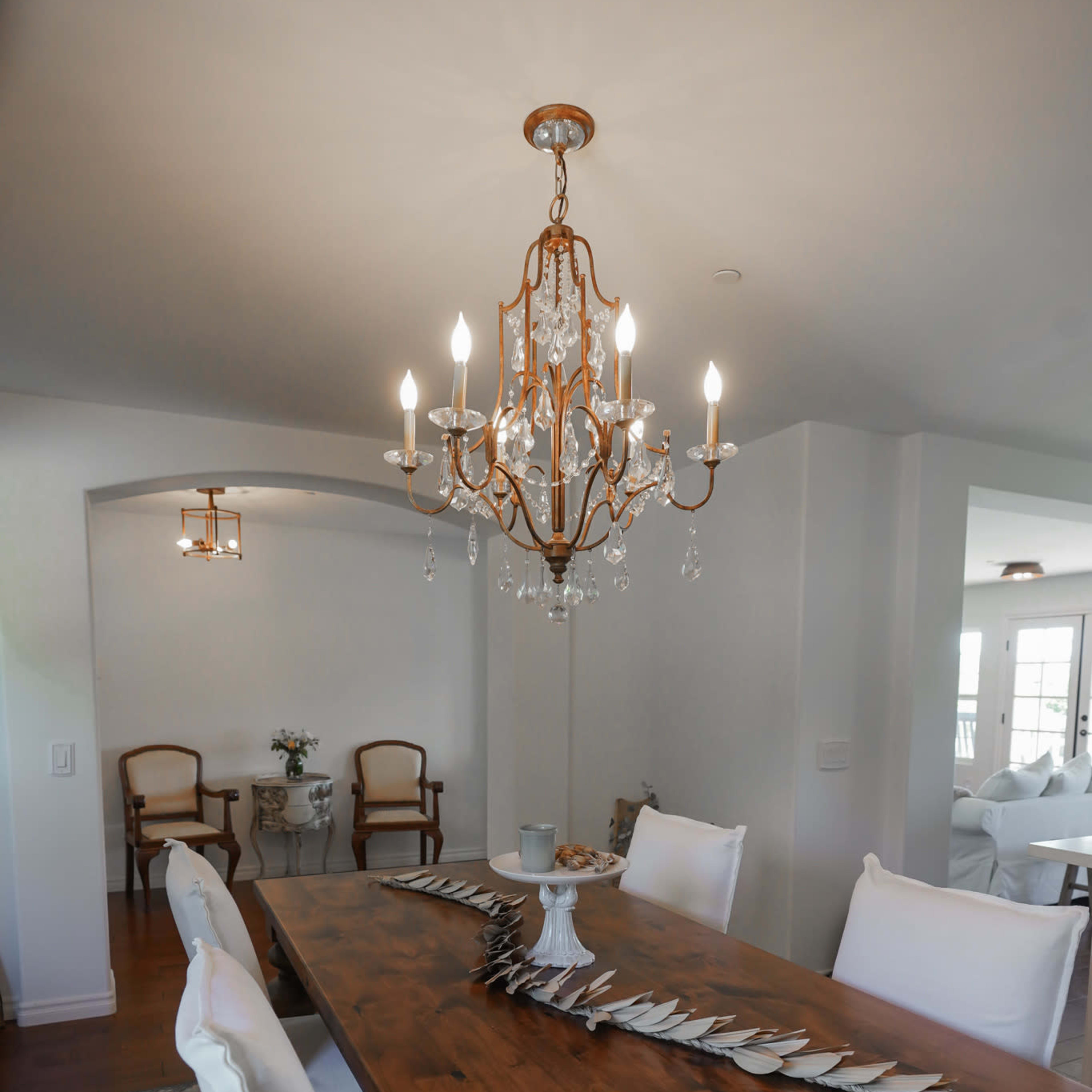 A wooden dining table with white chairs and a chandelier hangs above in a well-lit dining area.