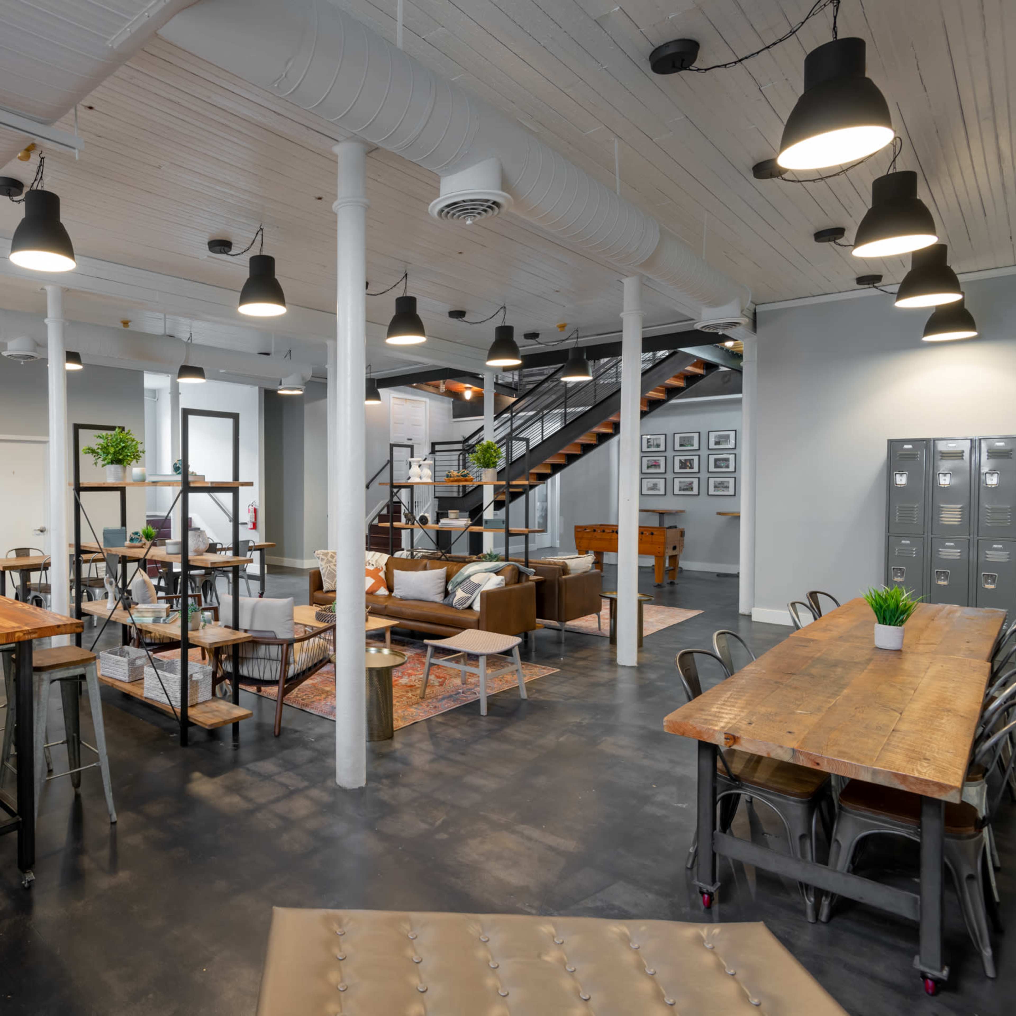 An industrial-style open office space with wooden furniture, metal shelving, and a staircase leading to an upper level.