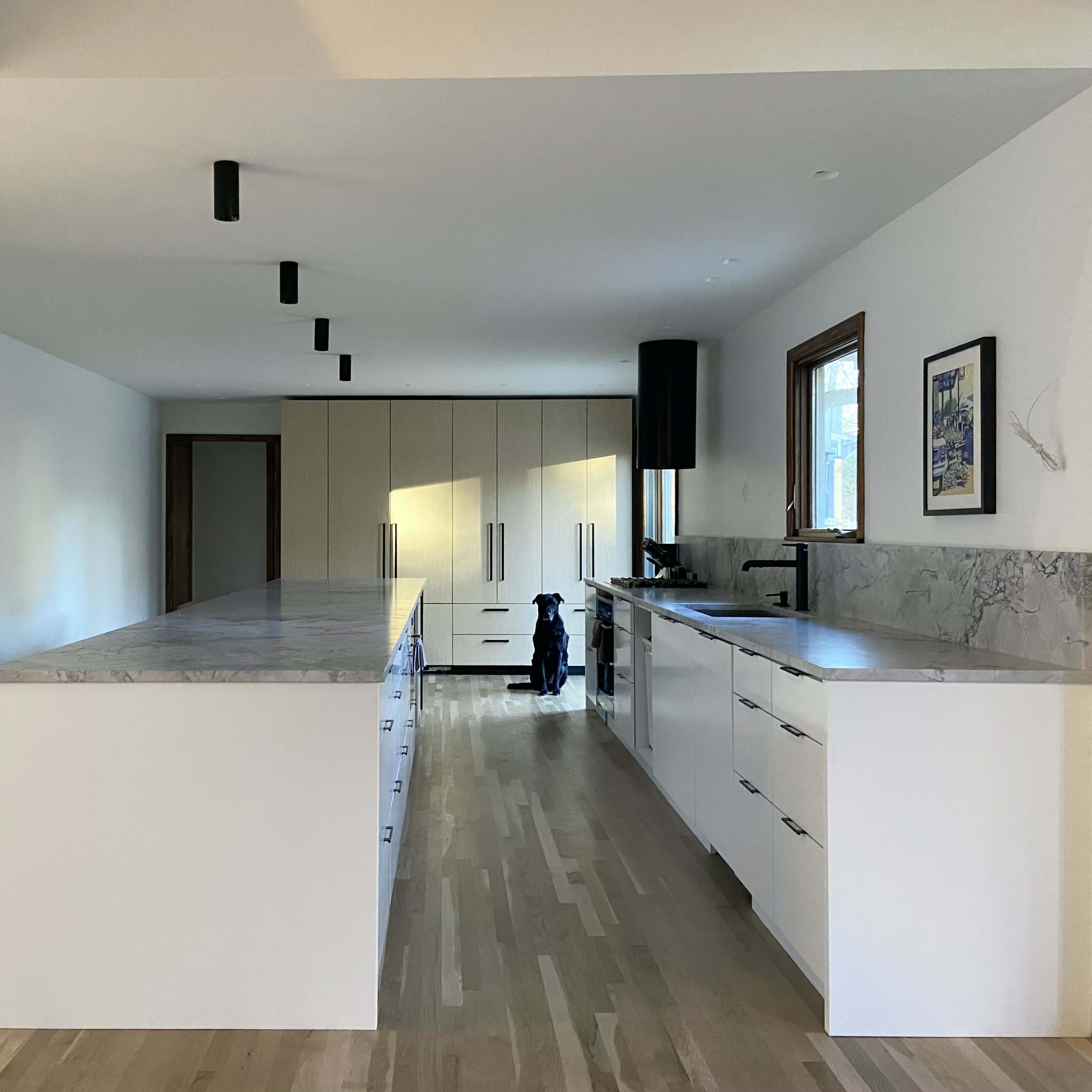 A spacious modern kitchen features a large island with marble countertops and sleek cabinetry, illuminated by black pendant lights.
