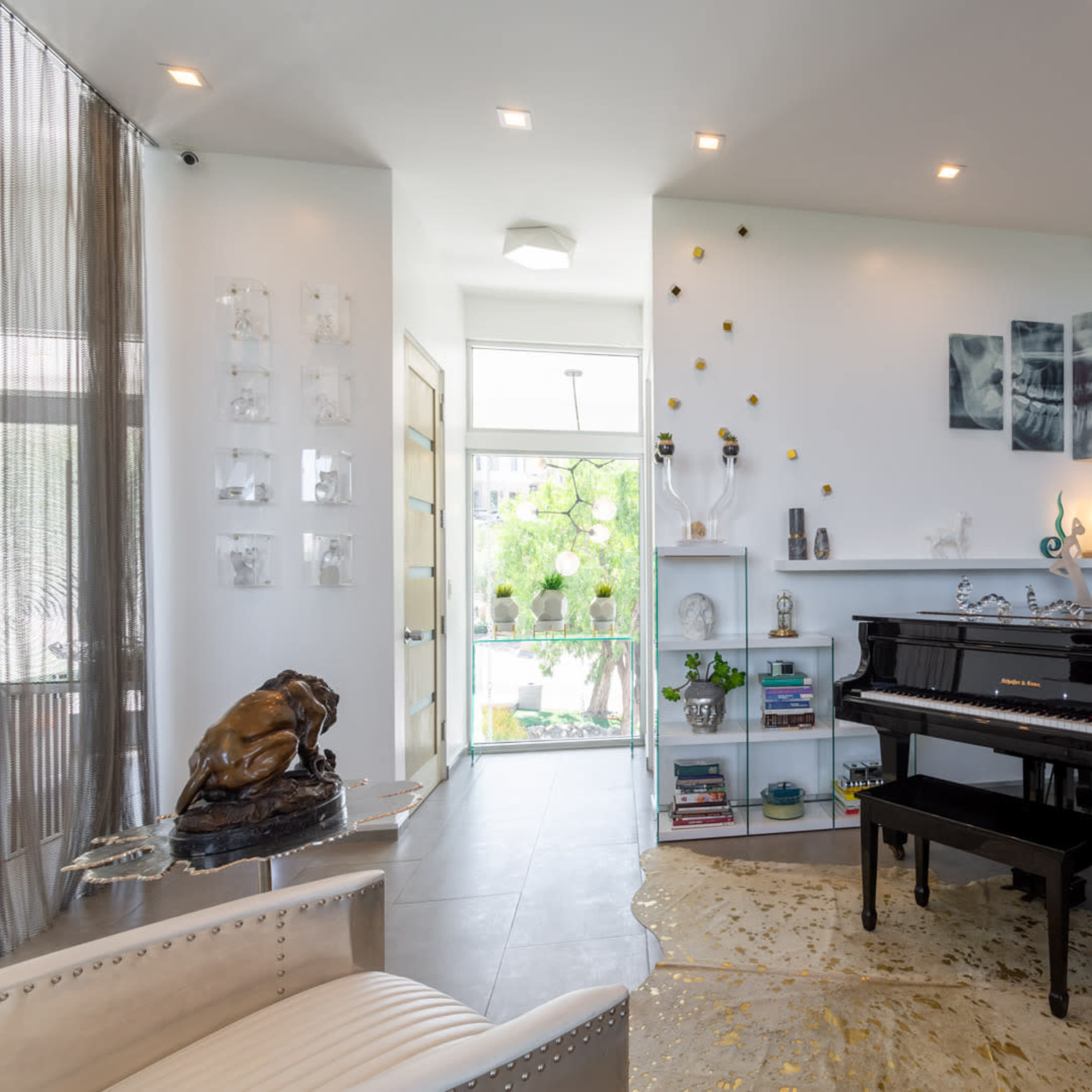 A modern room with a black grand piano positioned beside a wall adorned with decorative art and sculptures, while a large window provides natural light.