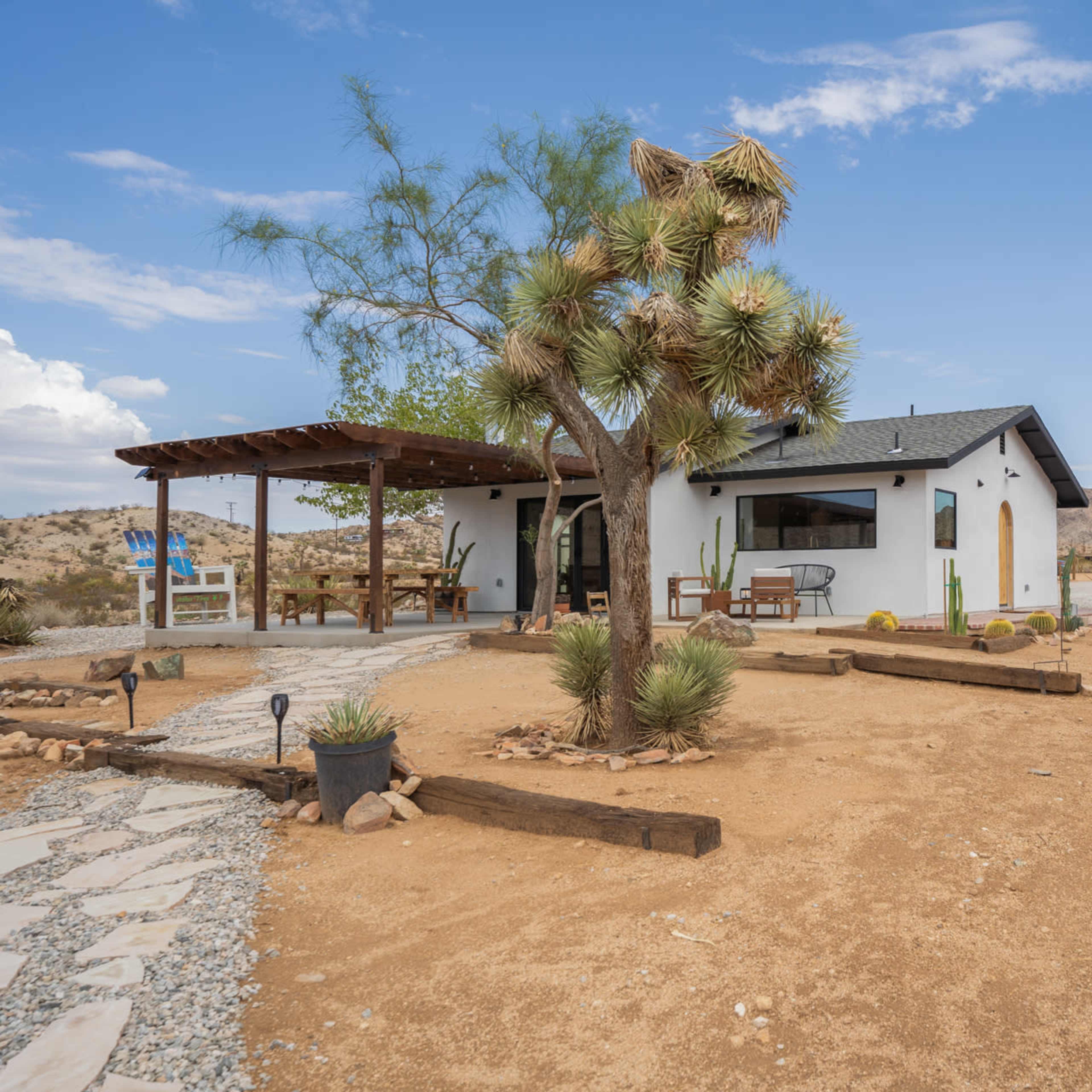 A single-story house with a covered porch is surrounded by desert landscaping and mountains in the background.