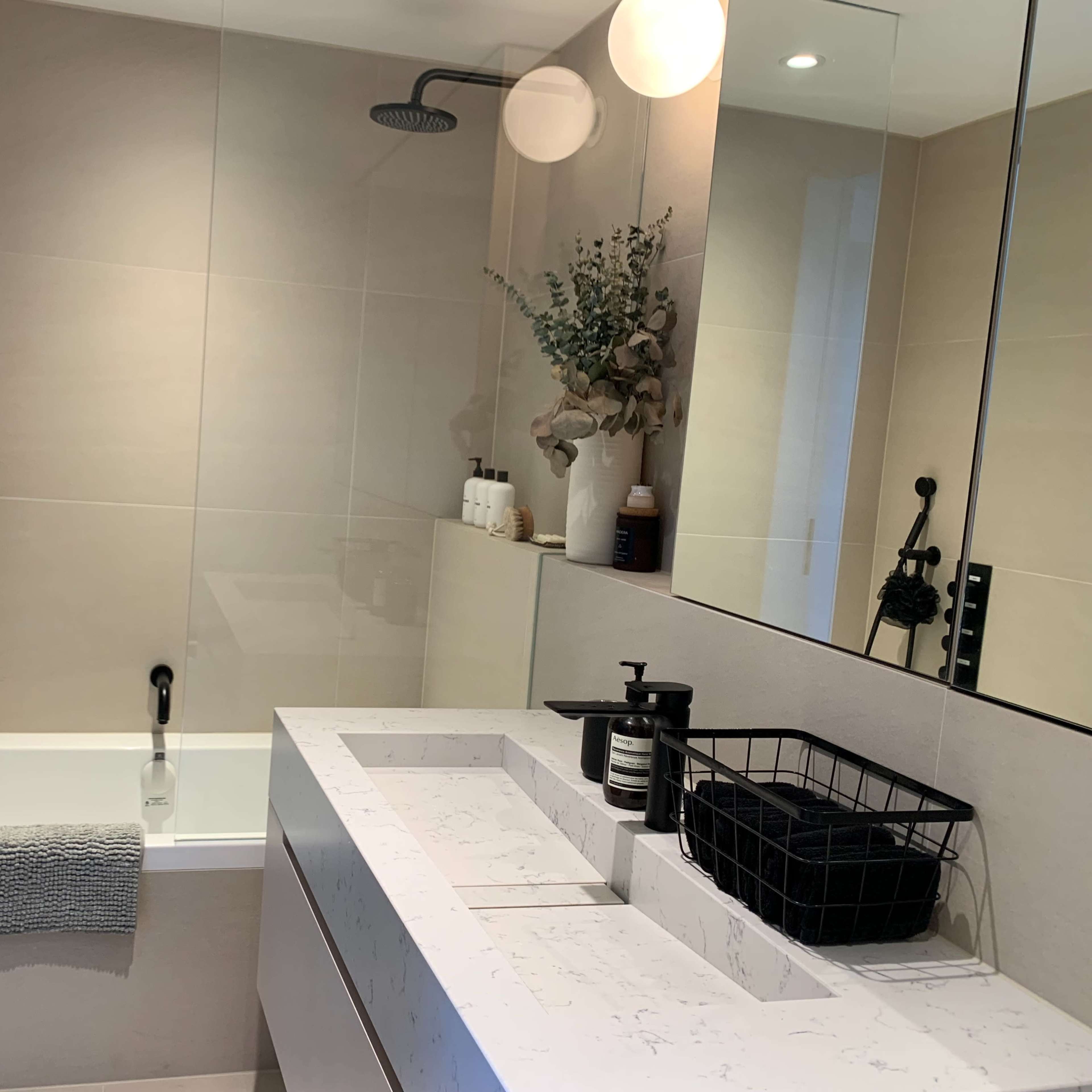 A modern bathroom featuring a bath with a showerhead, a marble countertop with a sink, and a mirror reflecting the space.