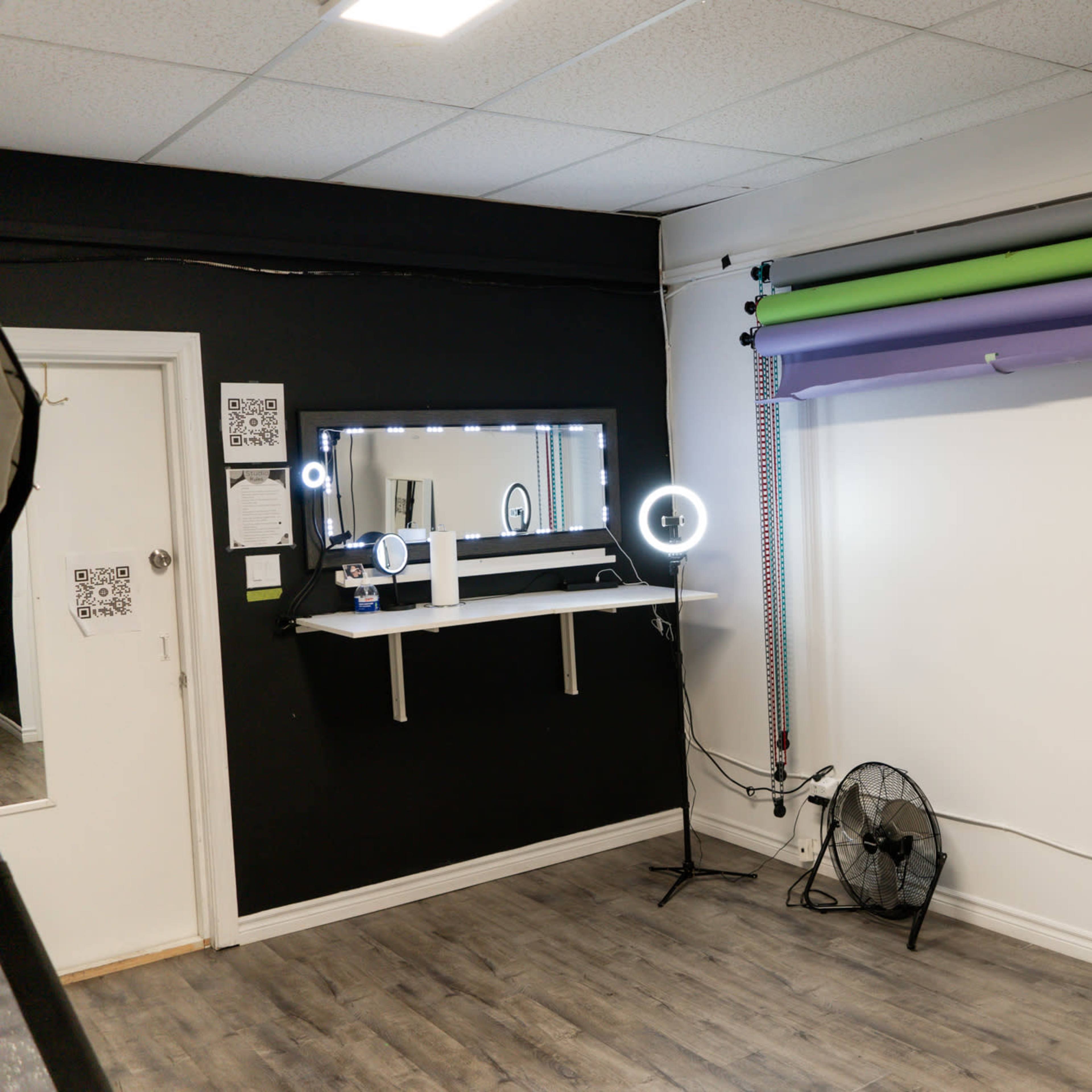 A photography studio featuring backdrops in green and purple, a mirror, softbox lights, and a circular light setup against a black wall.