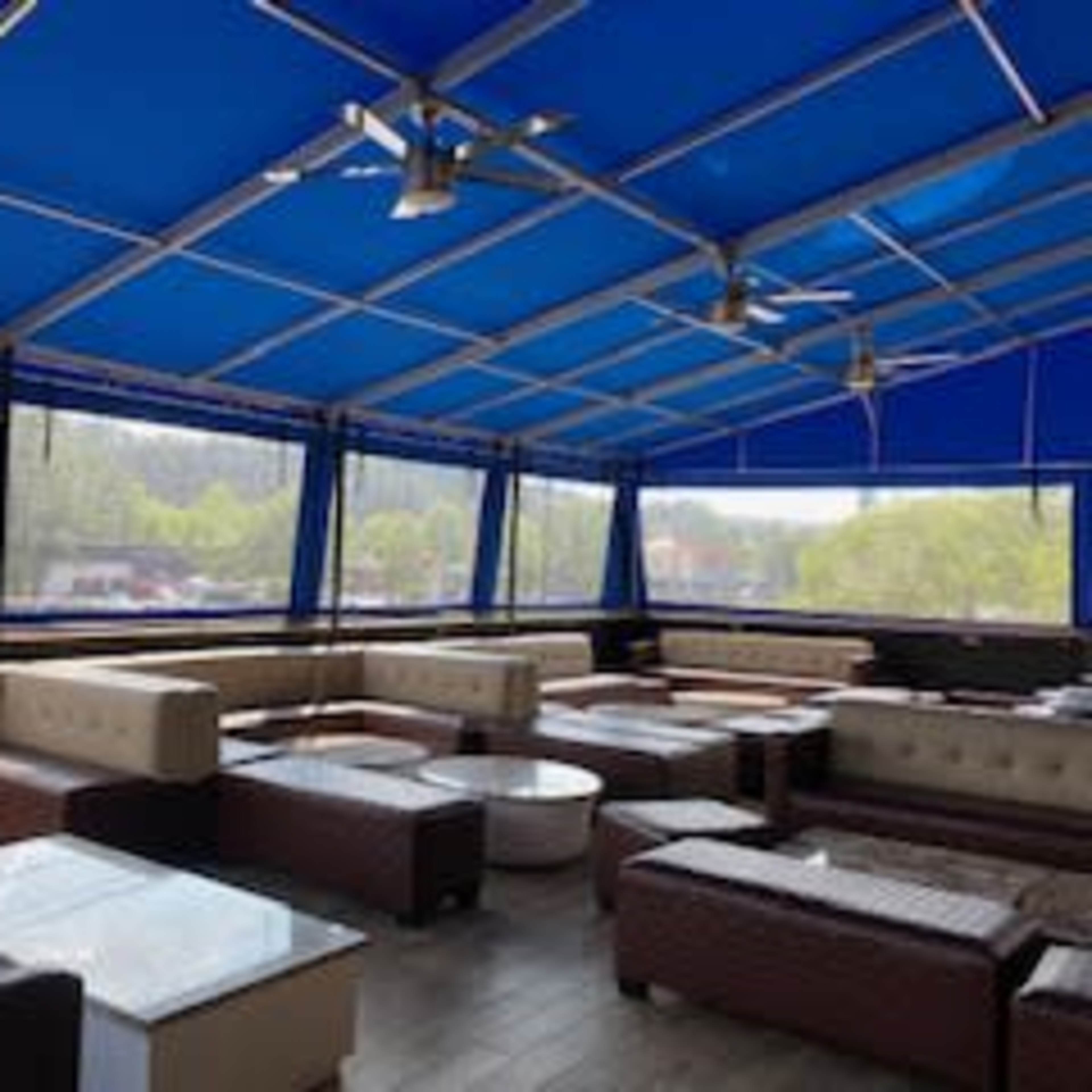 A covered outdoor seating area with several tables and couches arranged beneath a blue tent.