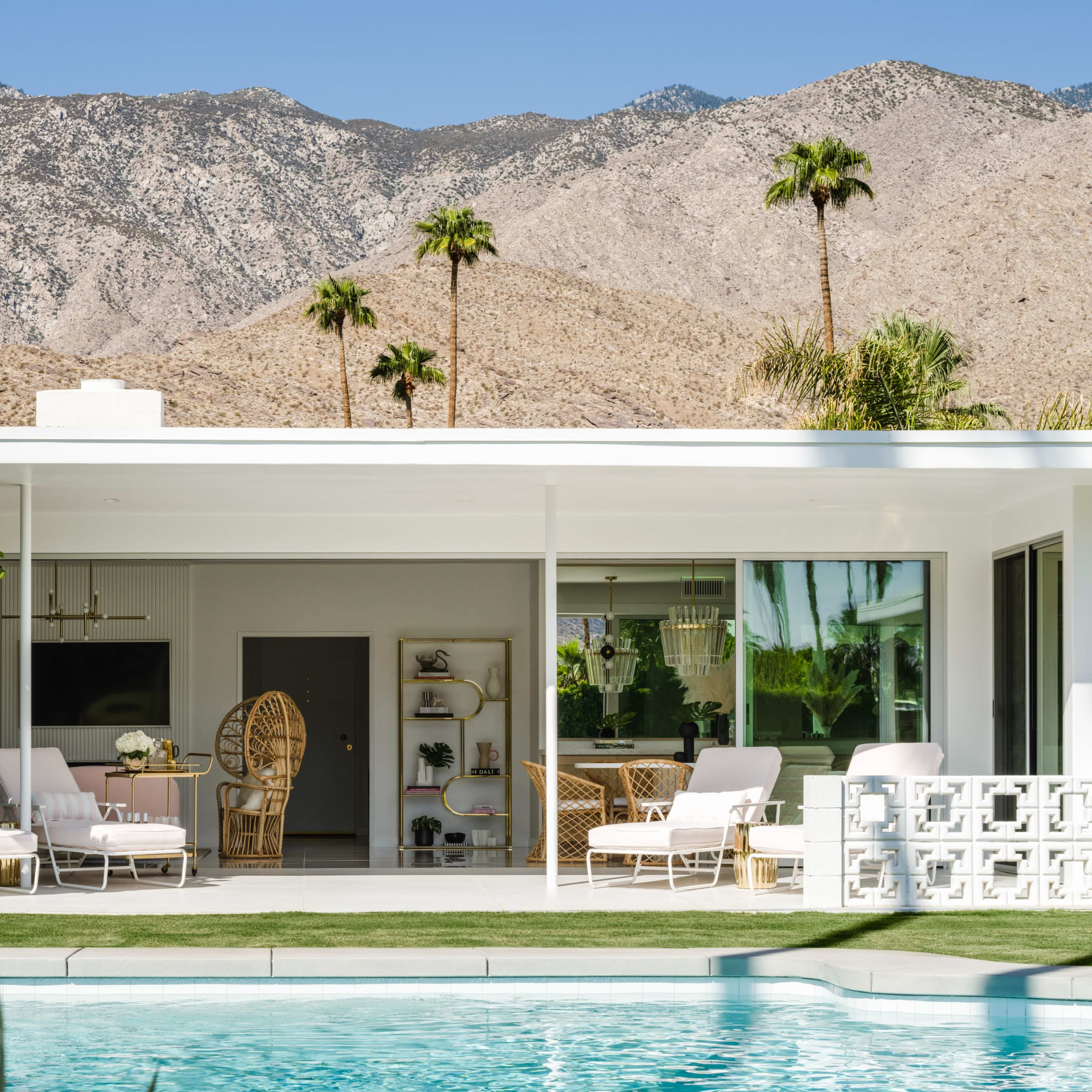 A modern house with a swimming pool features a patio with lounge chairs and views of a mountain landscape in the background.