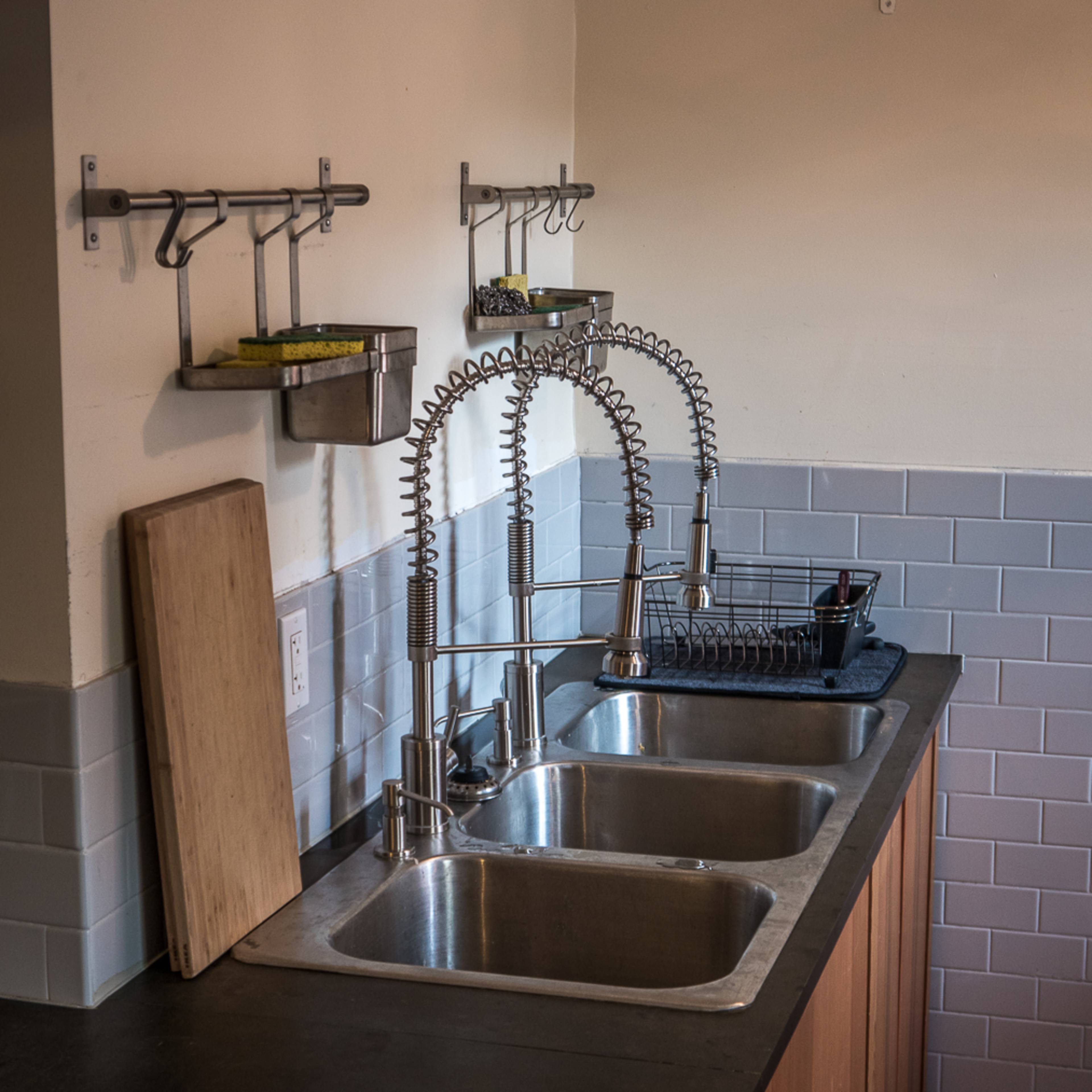 A kitchen with two stainless steel sinks, a wooden cutting board, and various utensils mounted on the wall.