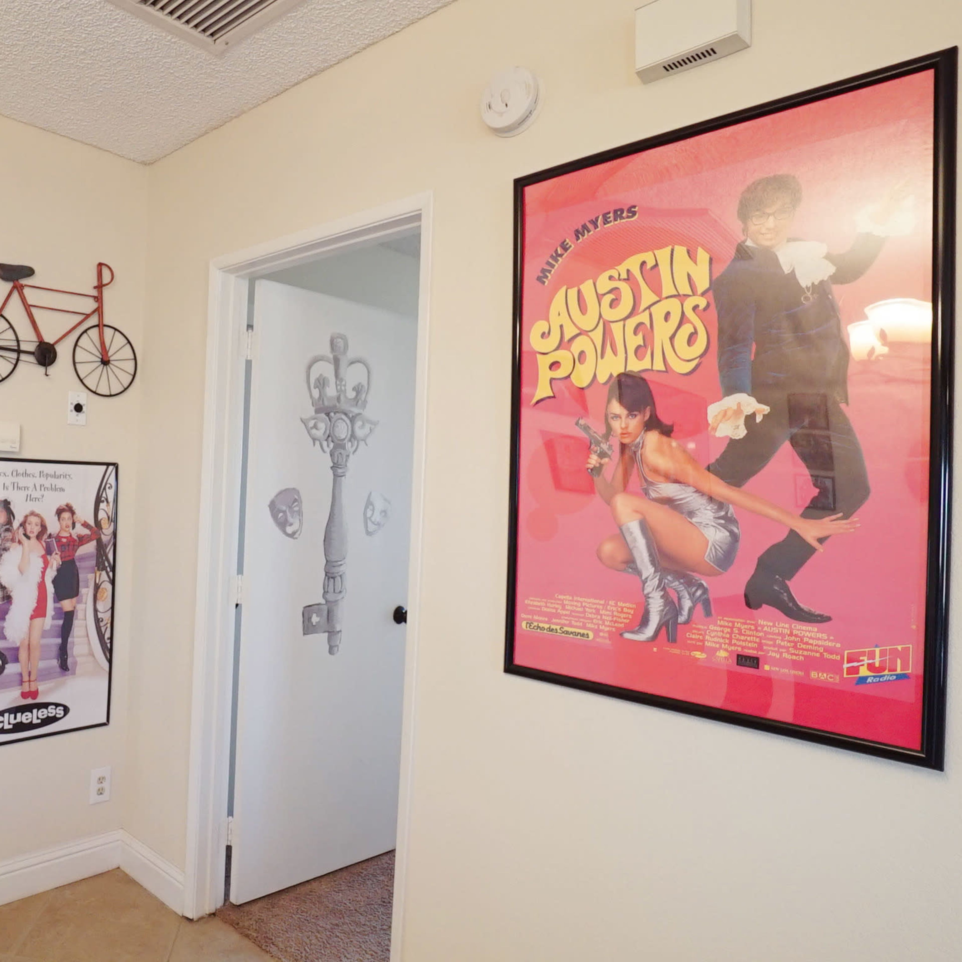 A hallway with two doors on the left and right, a bicycle decor hung on the wall, and framed movie posters, including one for "Austin Powers."
