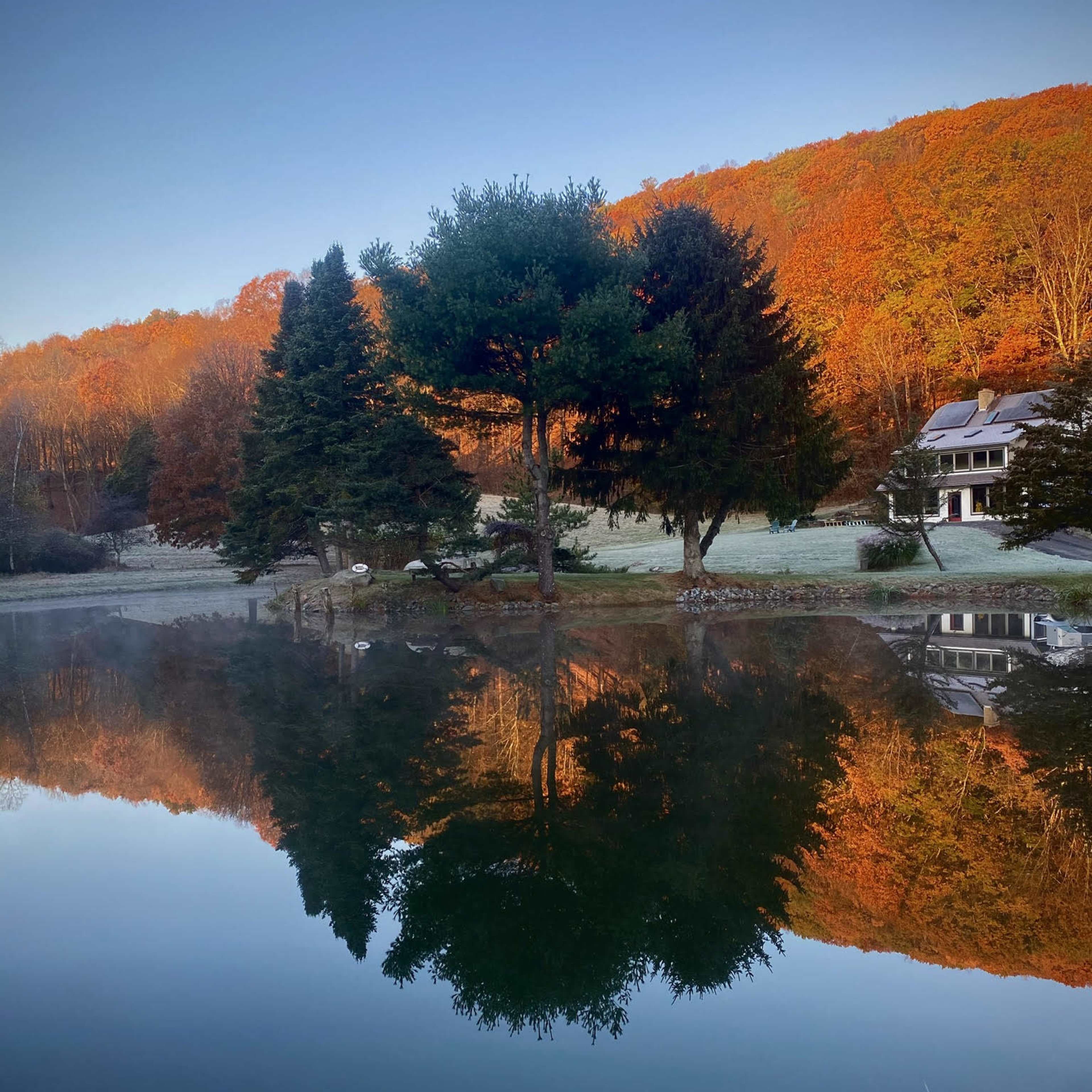 A serene lake reflecting colorful autumn trees and a house surrounded by a hillside.