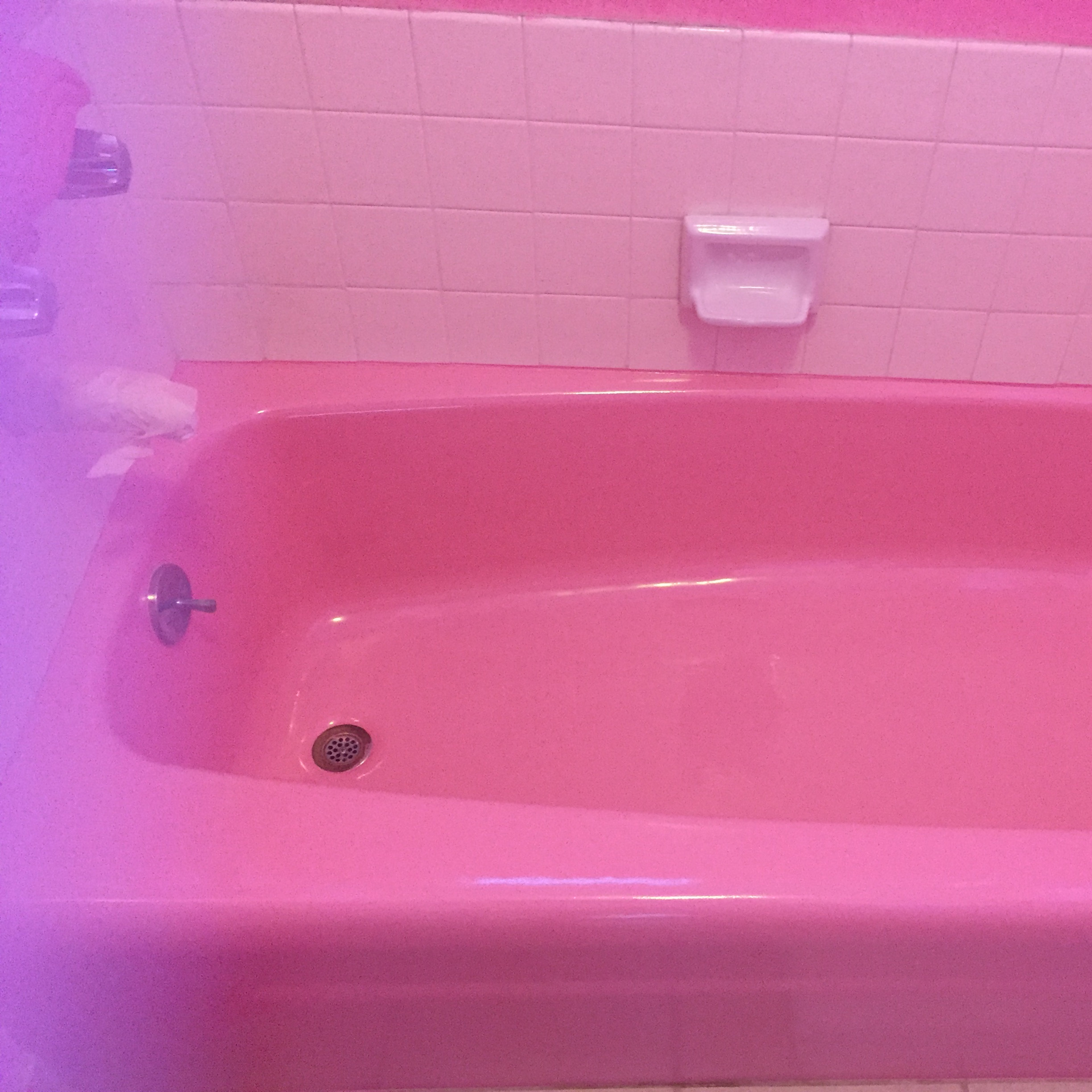 A pink bathtub set against a pink-tiled bathroom wall.