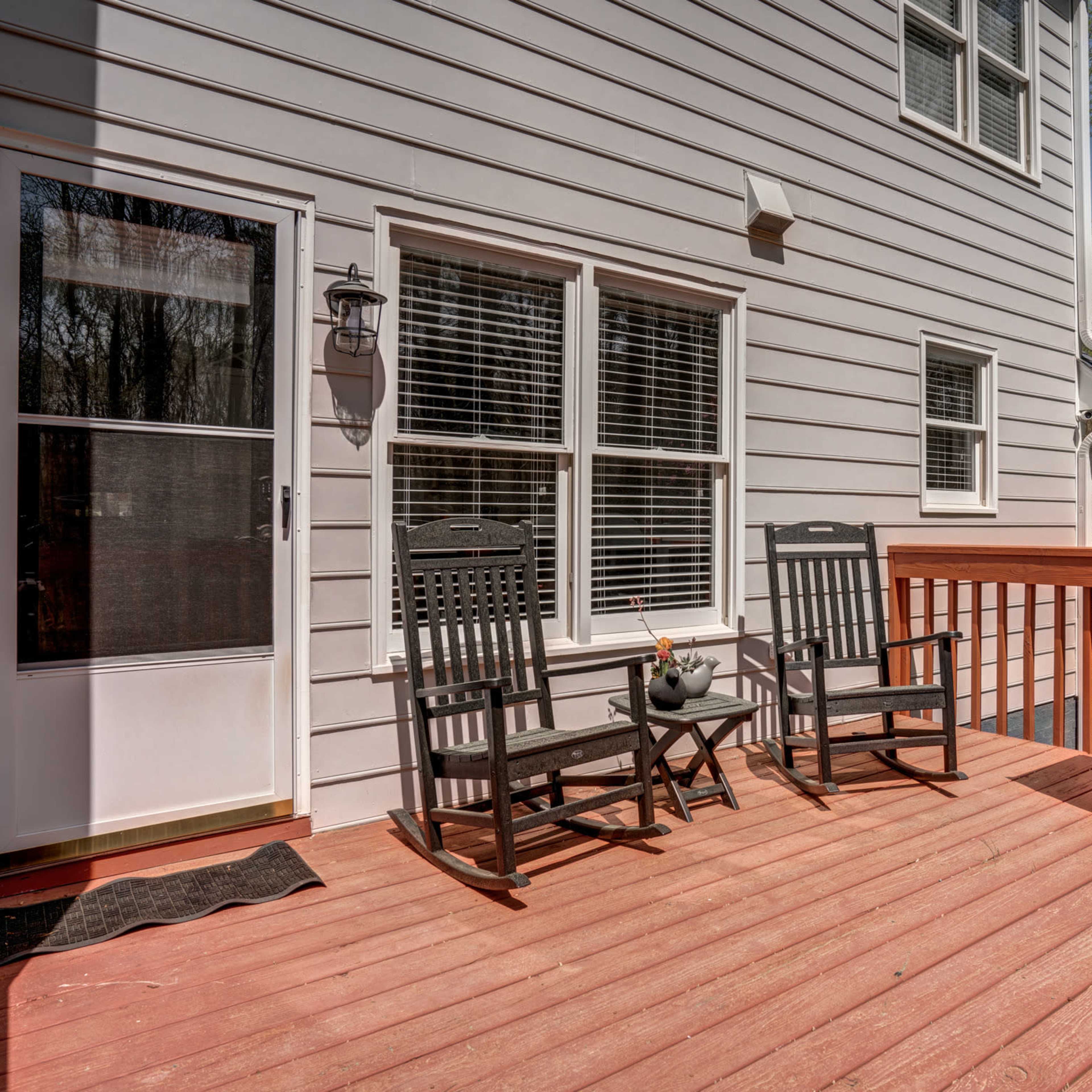 A wooden deck with two rocking chairs, a small table with a plant, and a gas grill, adjacent to a house with white siding.