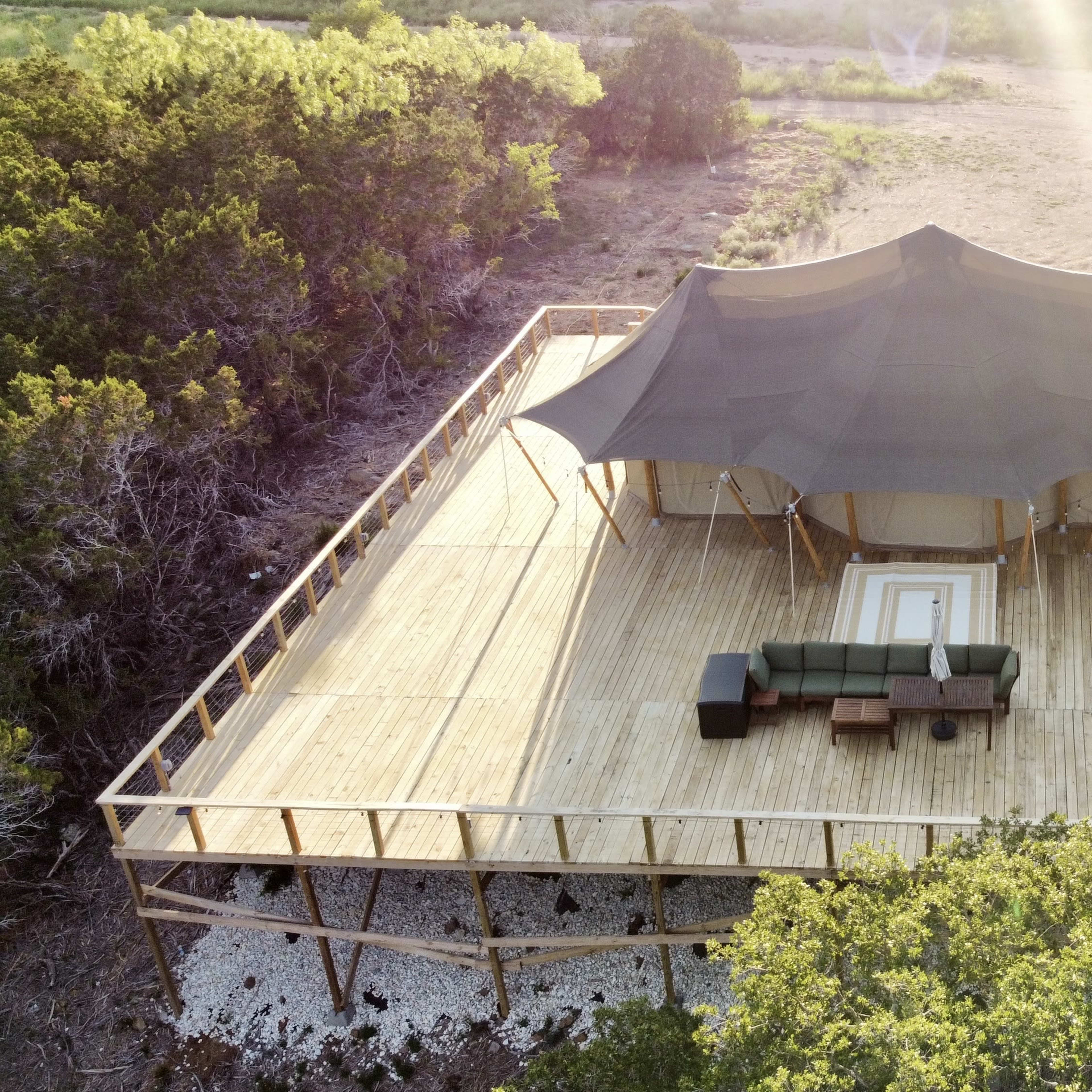 A large wooden deck features a tent structure with a seating area and is surrounded by a natural landscape.