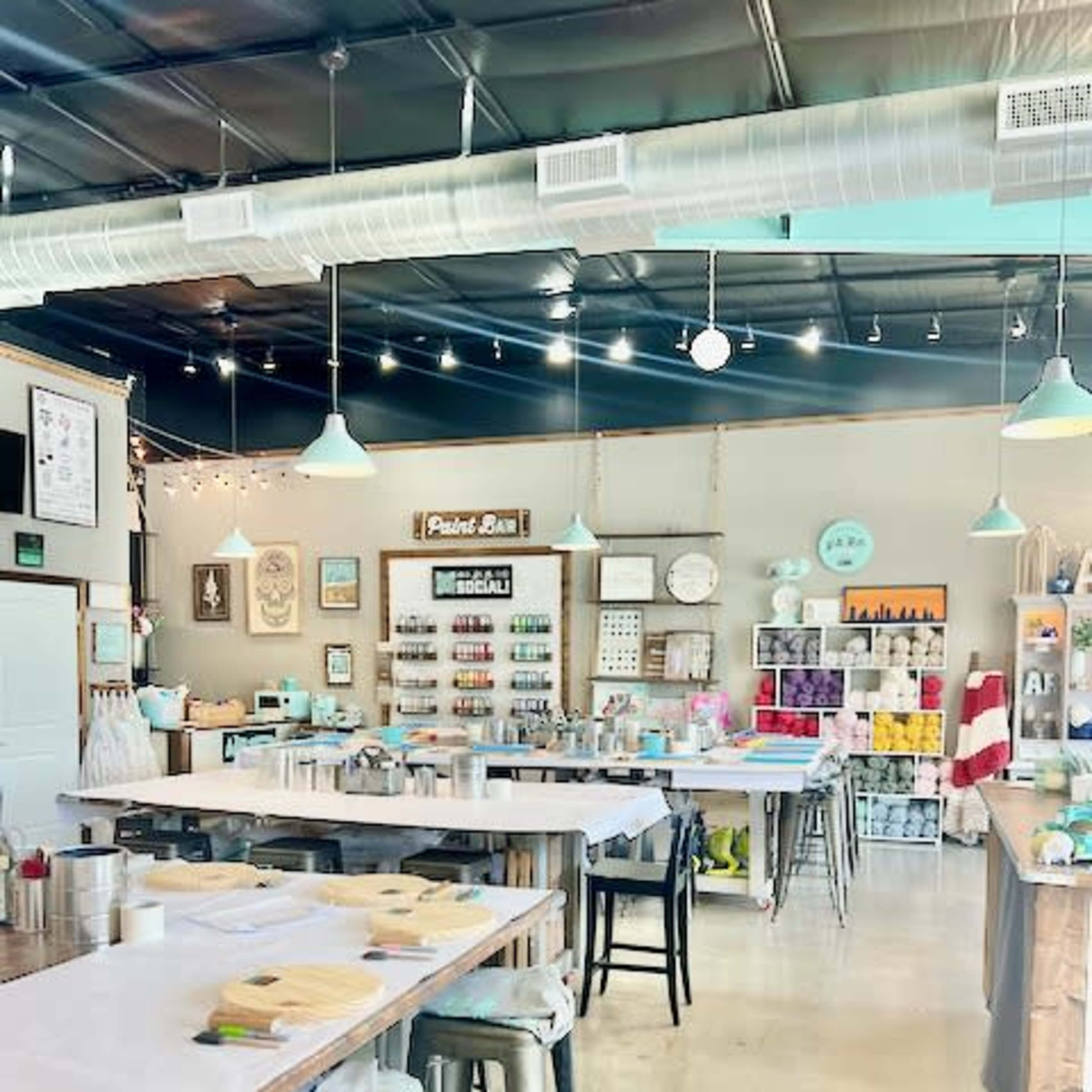 An art studio with neatly arranged tables, each equipped with painting supplies, and shelves displaying colorful craft materials.