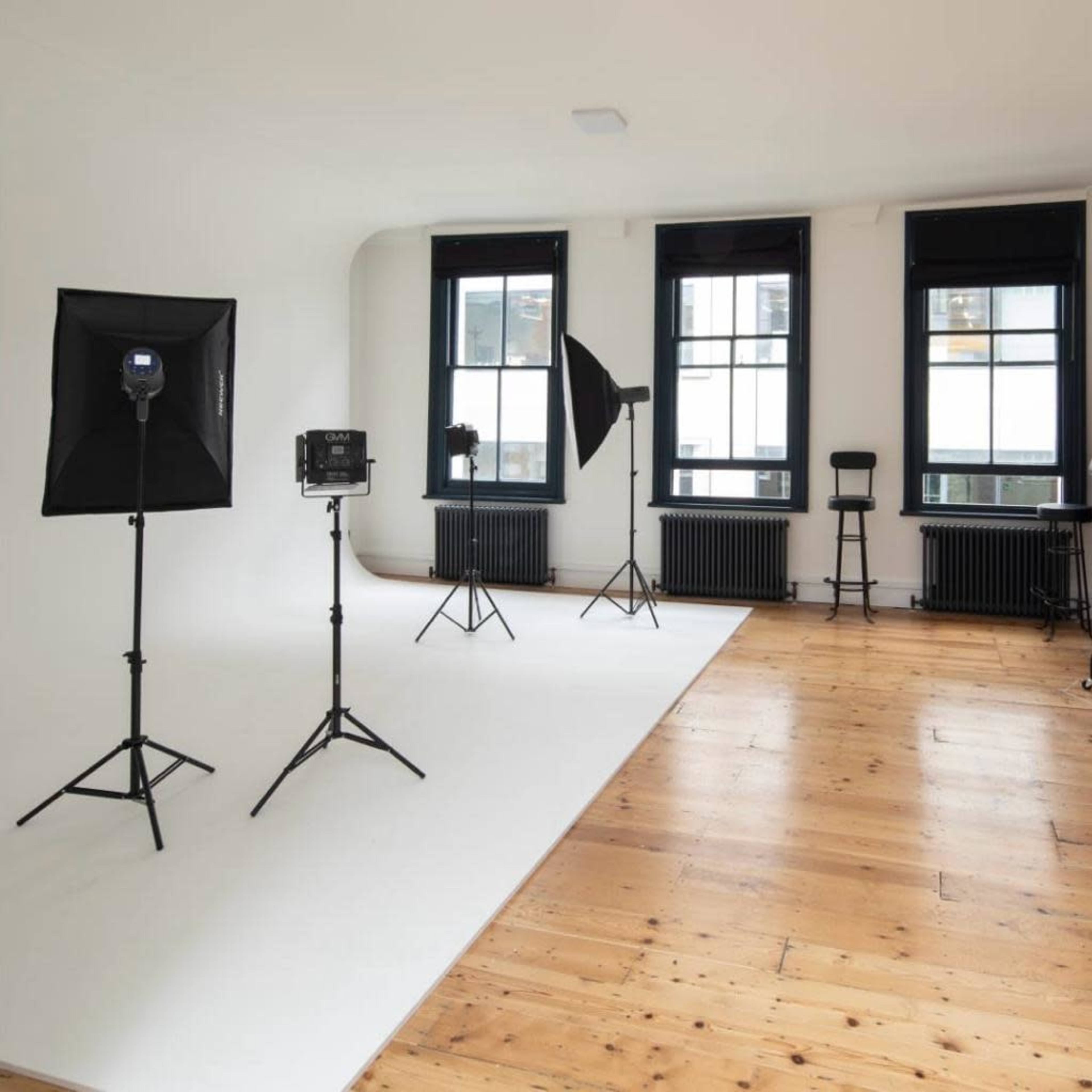 A photography studio with three lighting setups and large windows overlooking a minimalist wooden floor.