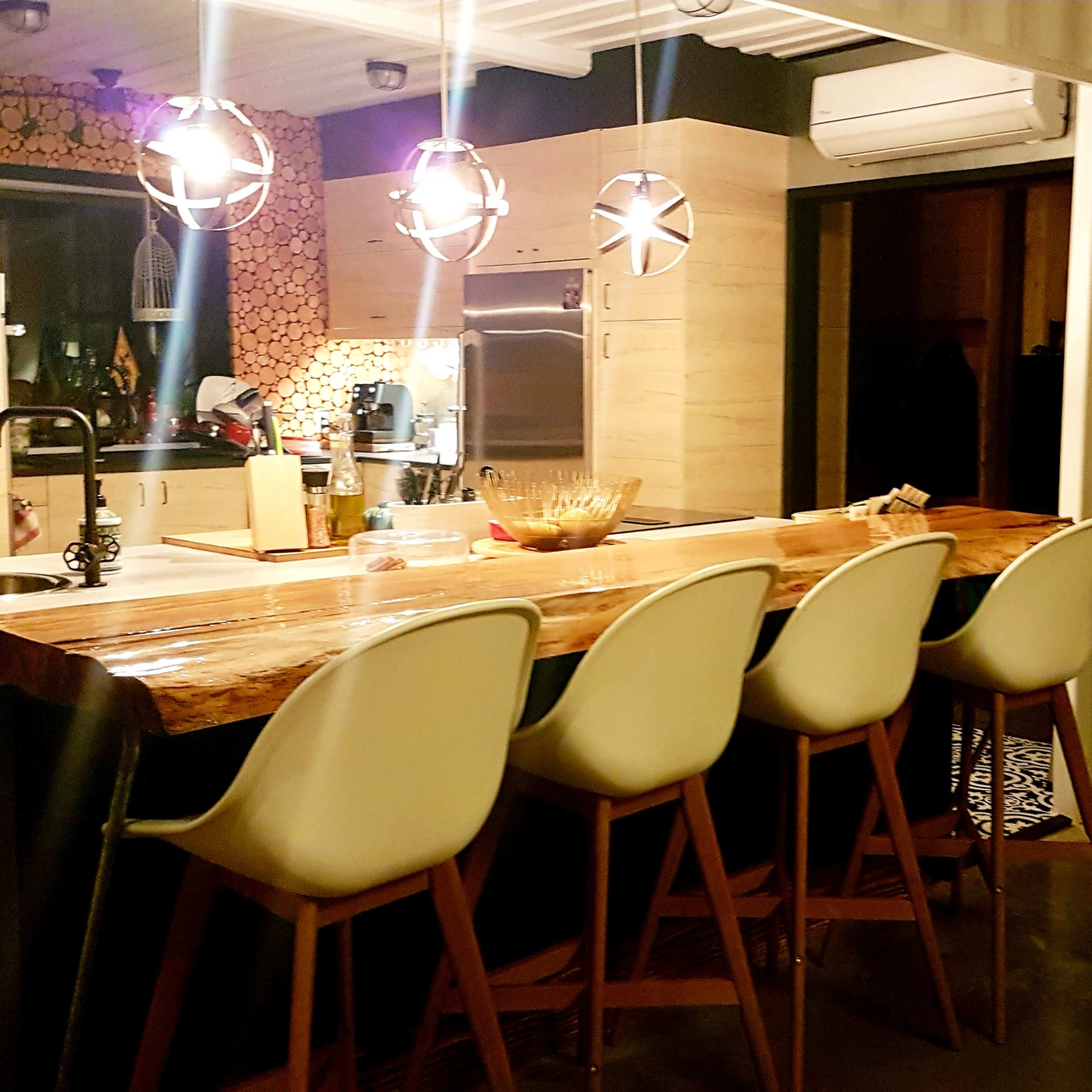 A modern kitchen with a wooden bar counter and five white chairs, featuring pendant lights above and a stylish interior design.