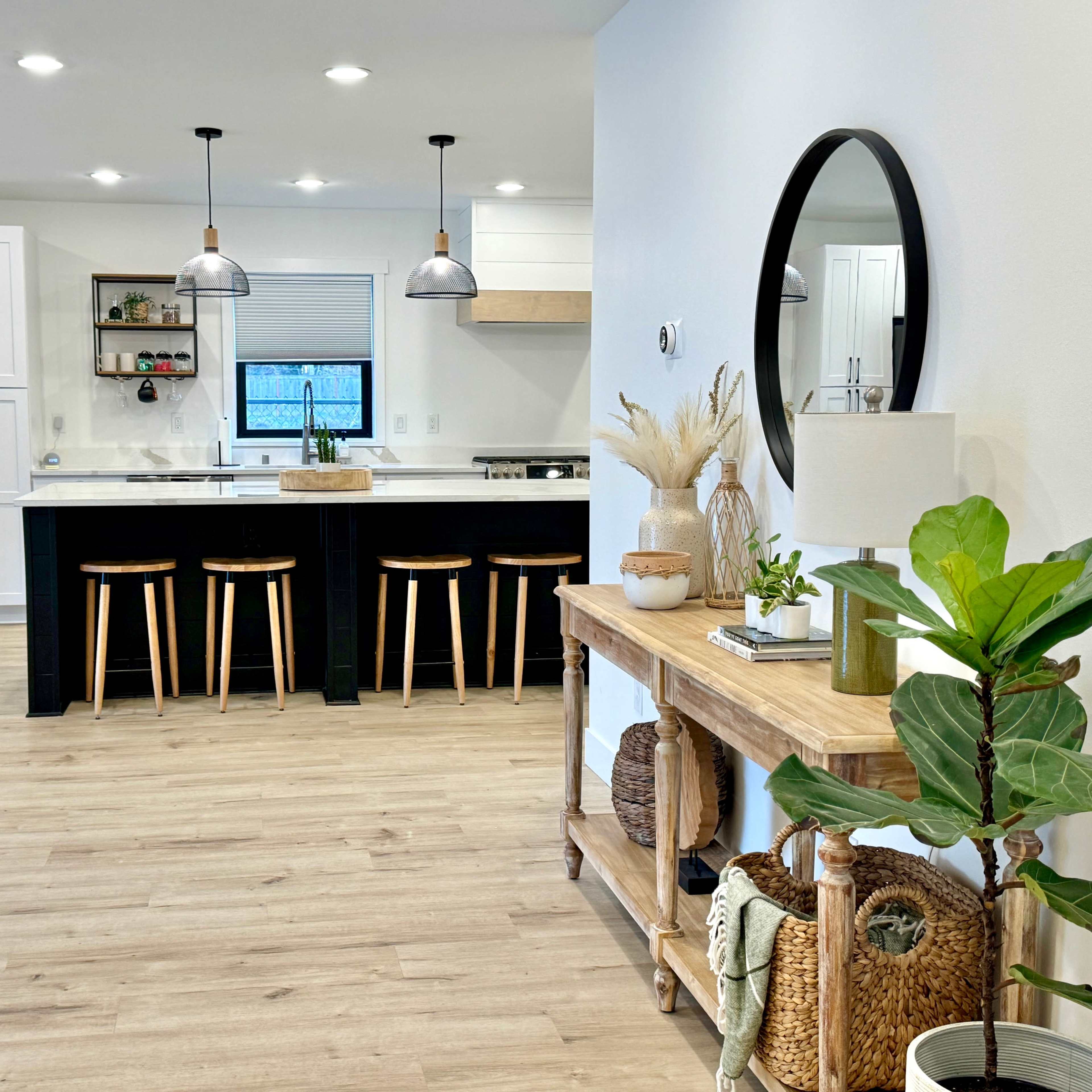 A modern kitchen and dining area features a white countertop, black island with stools, stainless steel appliances, and light wood flooring.