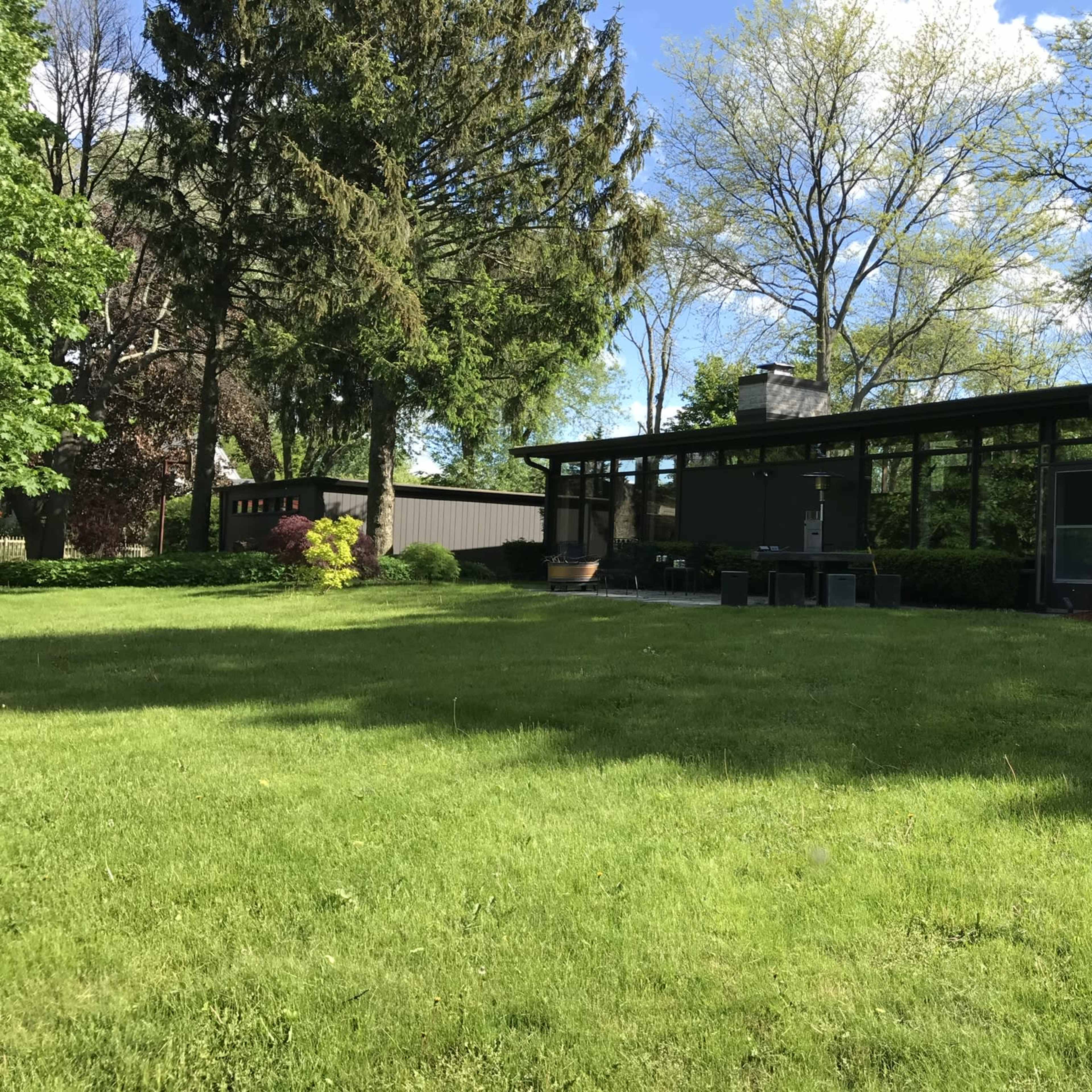 A modern house with large windows is situated on a grassy lawn surrounded by trees.