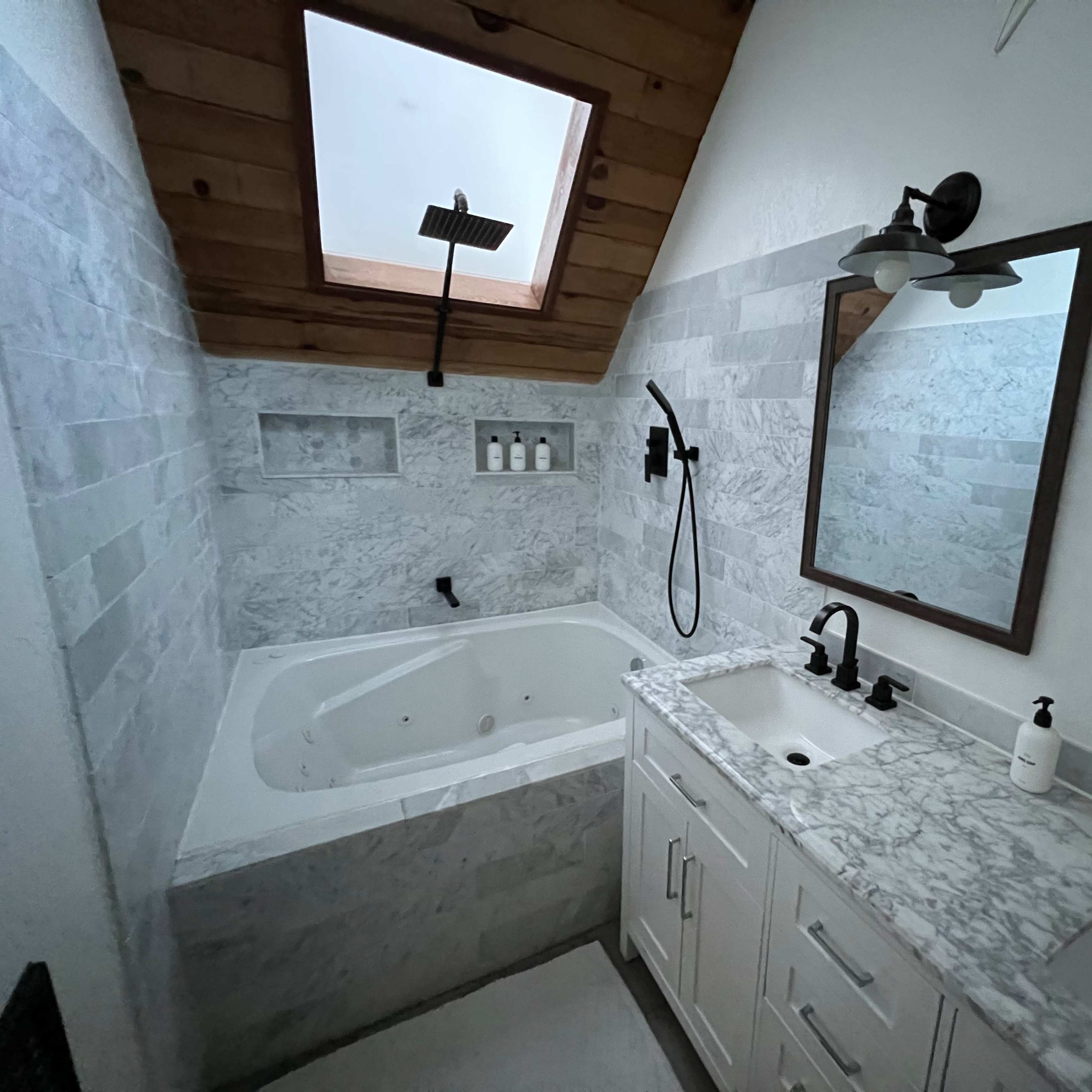 A bathroom featuring a marble-tiled shower area with a soaking tub, a dual sink vanity with modern fixtures, and a skylight above.