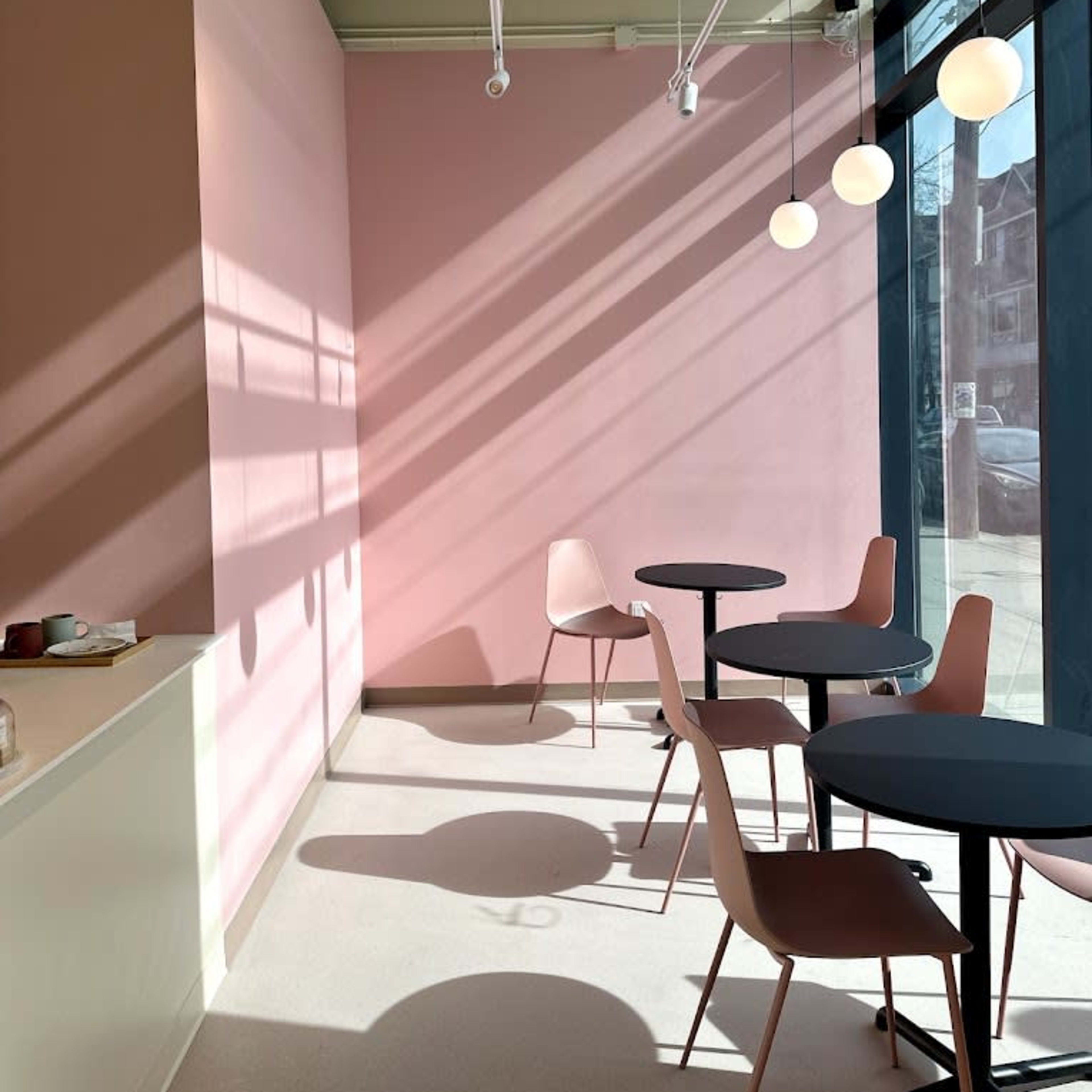 A modern café interior with pink walls, two round tables, and four pendant lights casting shadows on the floor.