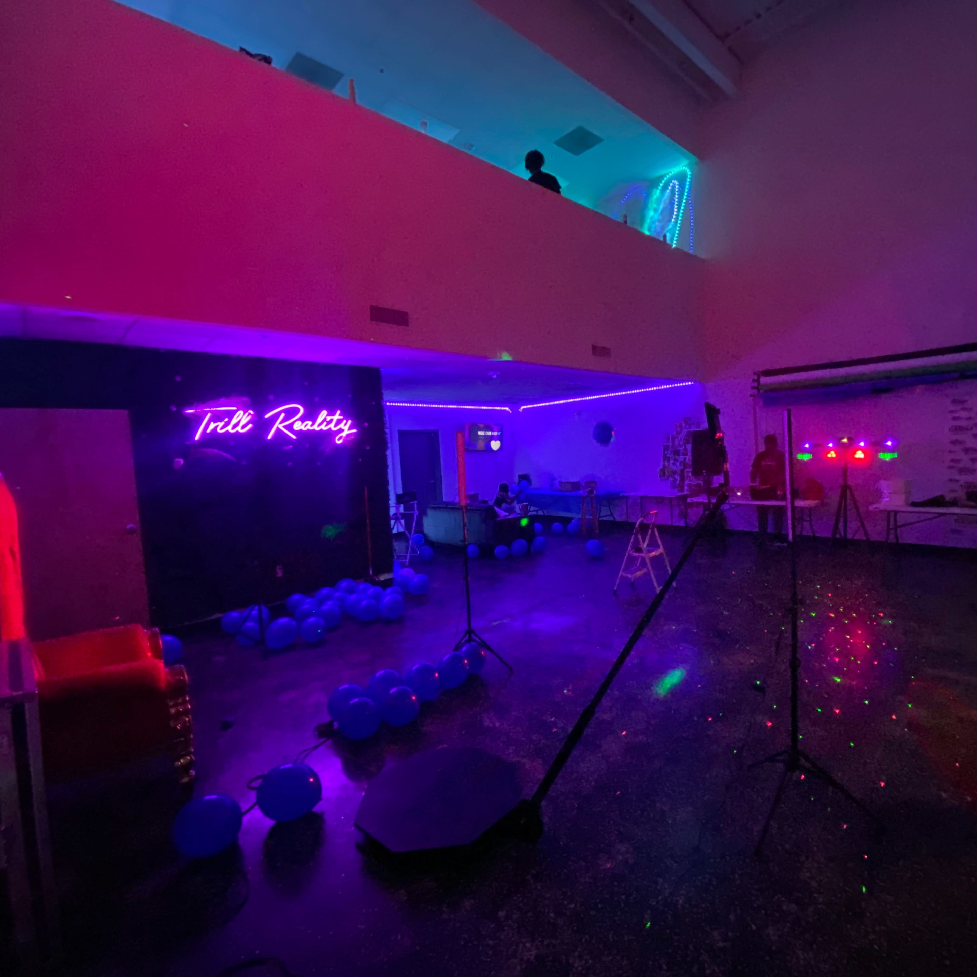 A spacious, dimly lit room with colorful neon lighting, decorations, and scattered blue balloons.