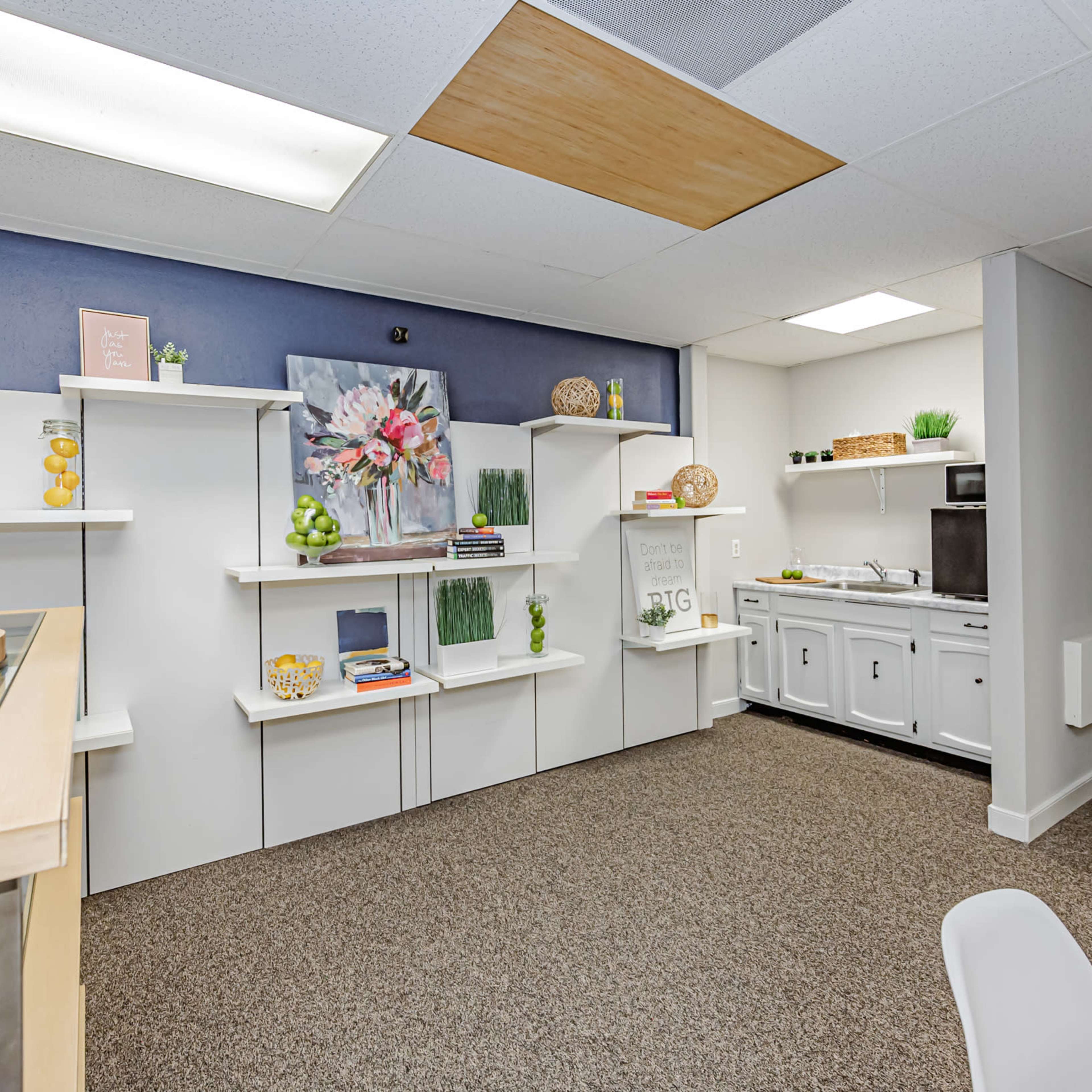 A neatly organized office space with white shelving, a kitchenette area, and a door leading to a restroom.