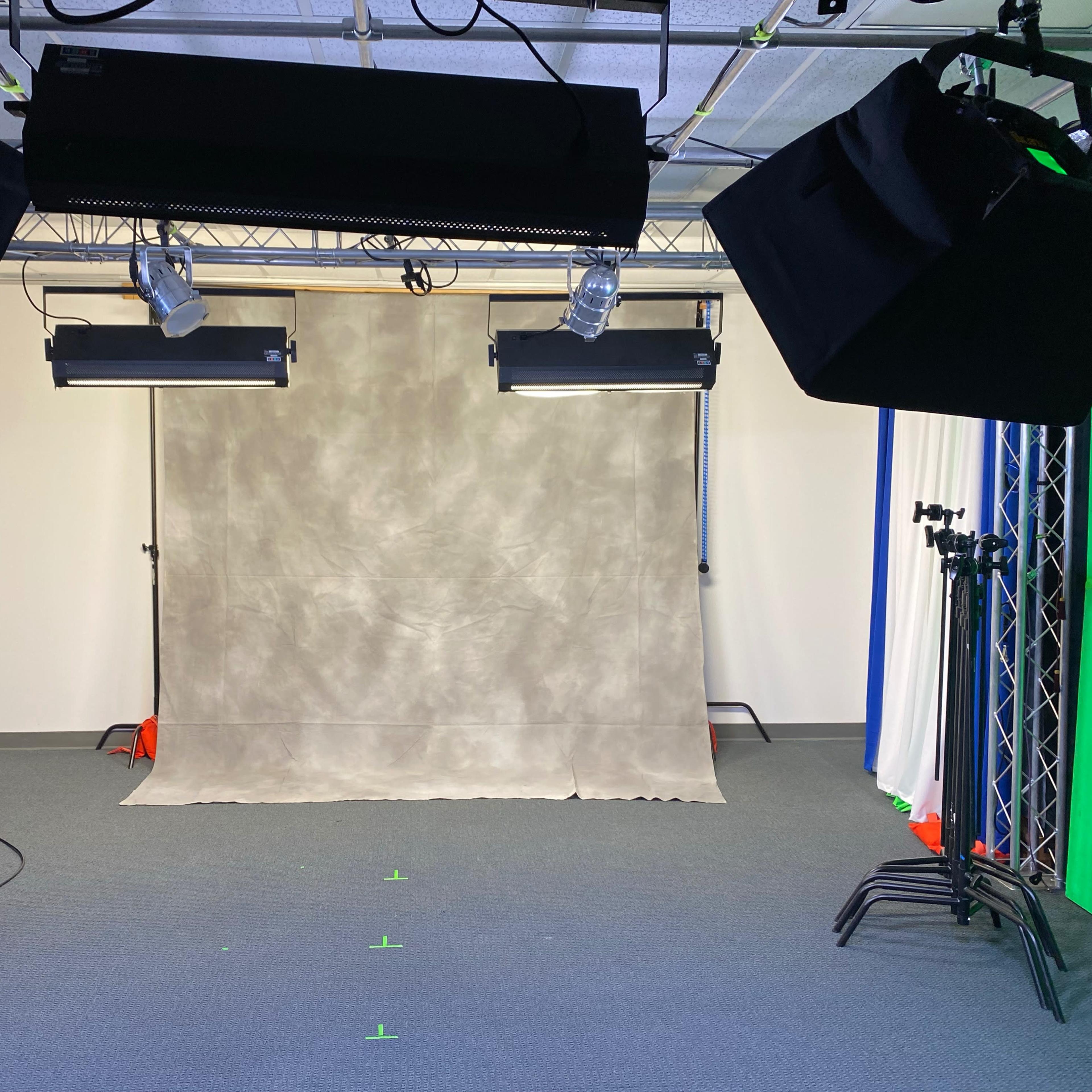 A photography studio setup with a gray backdrop, lighting equipment, and a green screen to the side.
