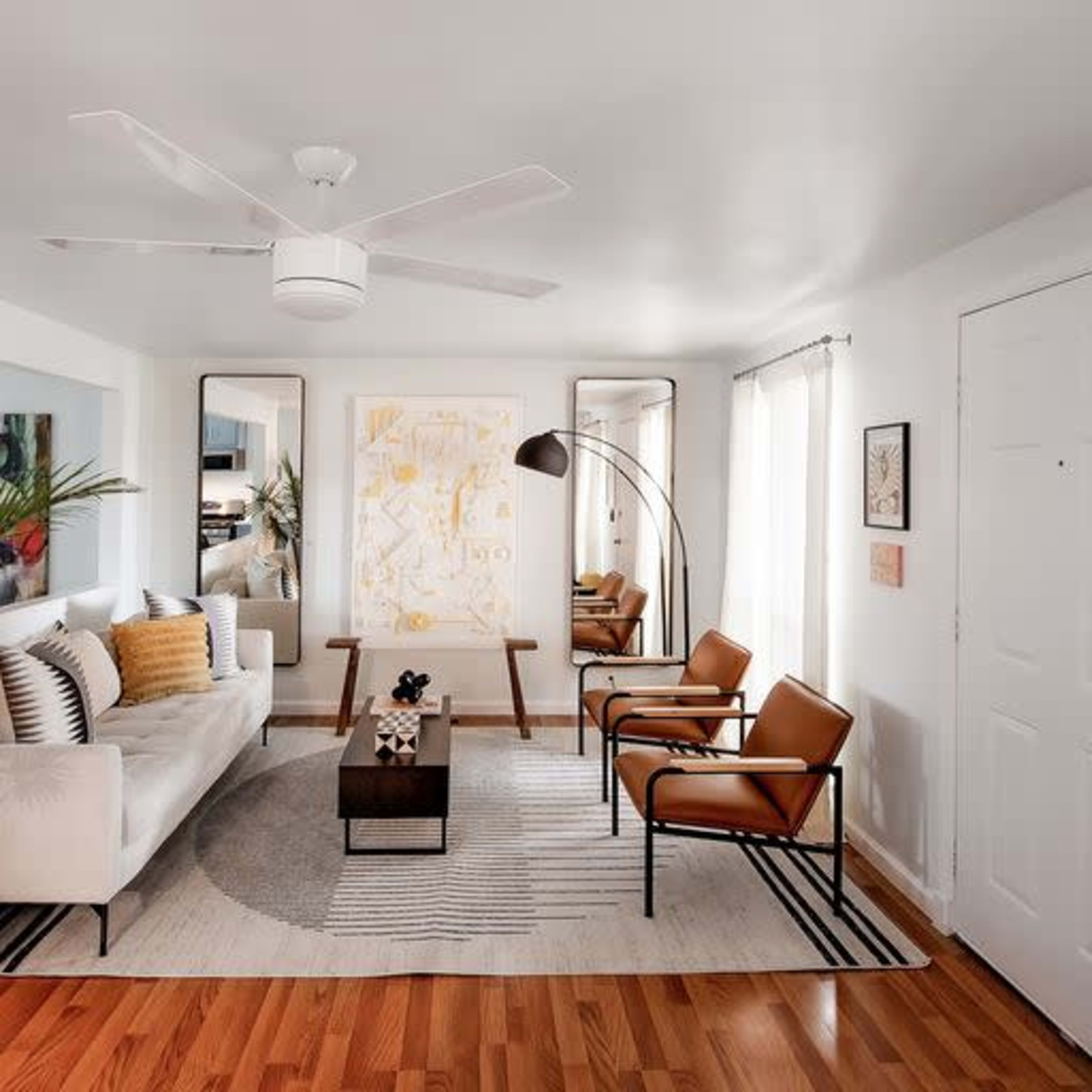 A modern living room with a white sofa, two brown chairs, a coffee table, and large windows allowing natural light.