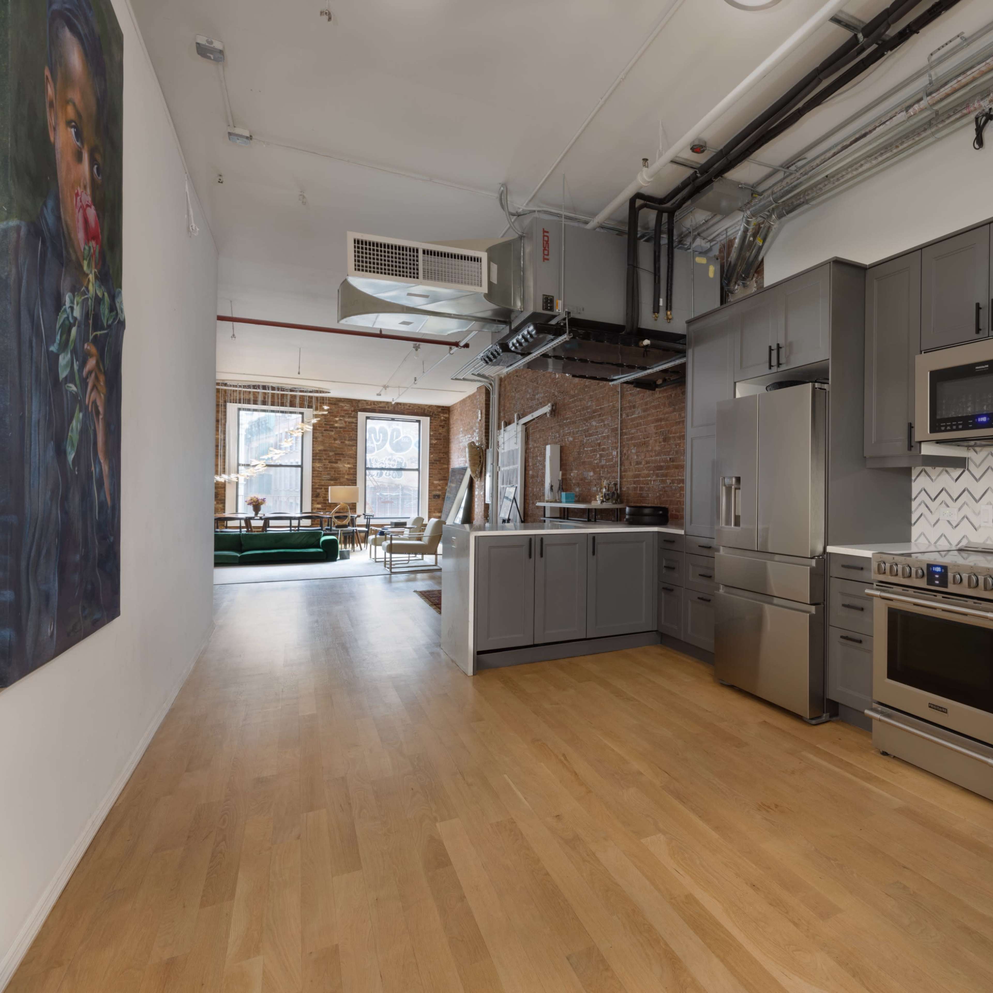 A modern kitchen with gray cabinetry, stainless steel appliances, and a herringbone tile backsplash, leading into a spacious open living area.