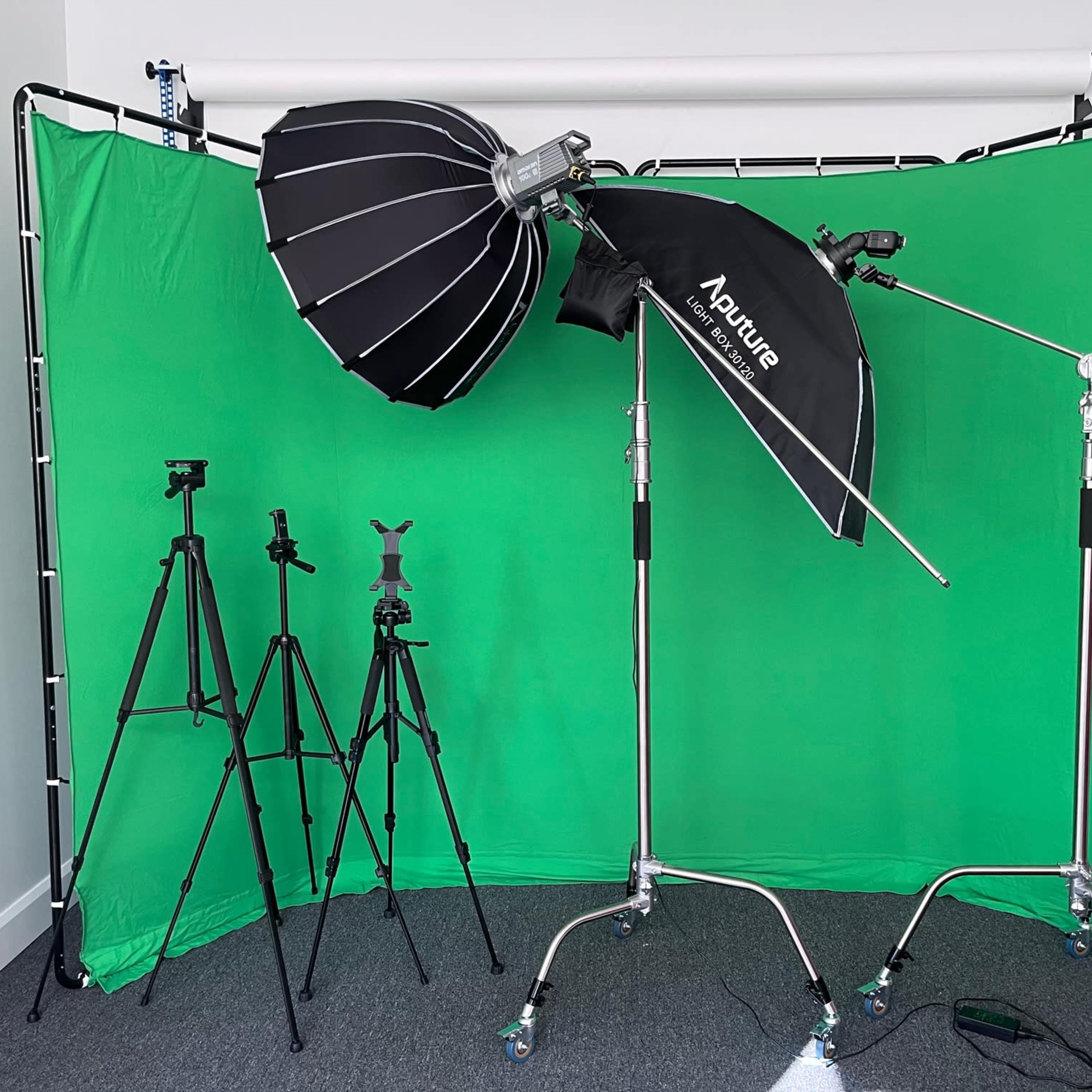 A photography setup with a green backdrop, softbox lights, and several tripods positioned on a carpeted floor.