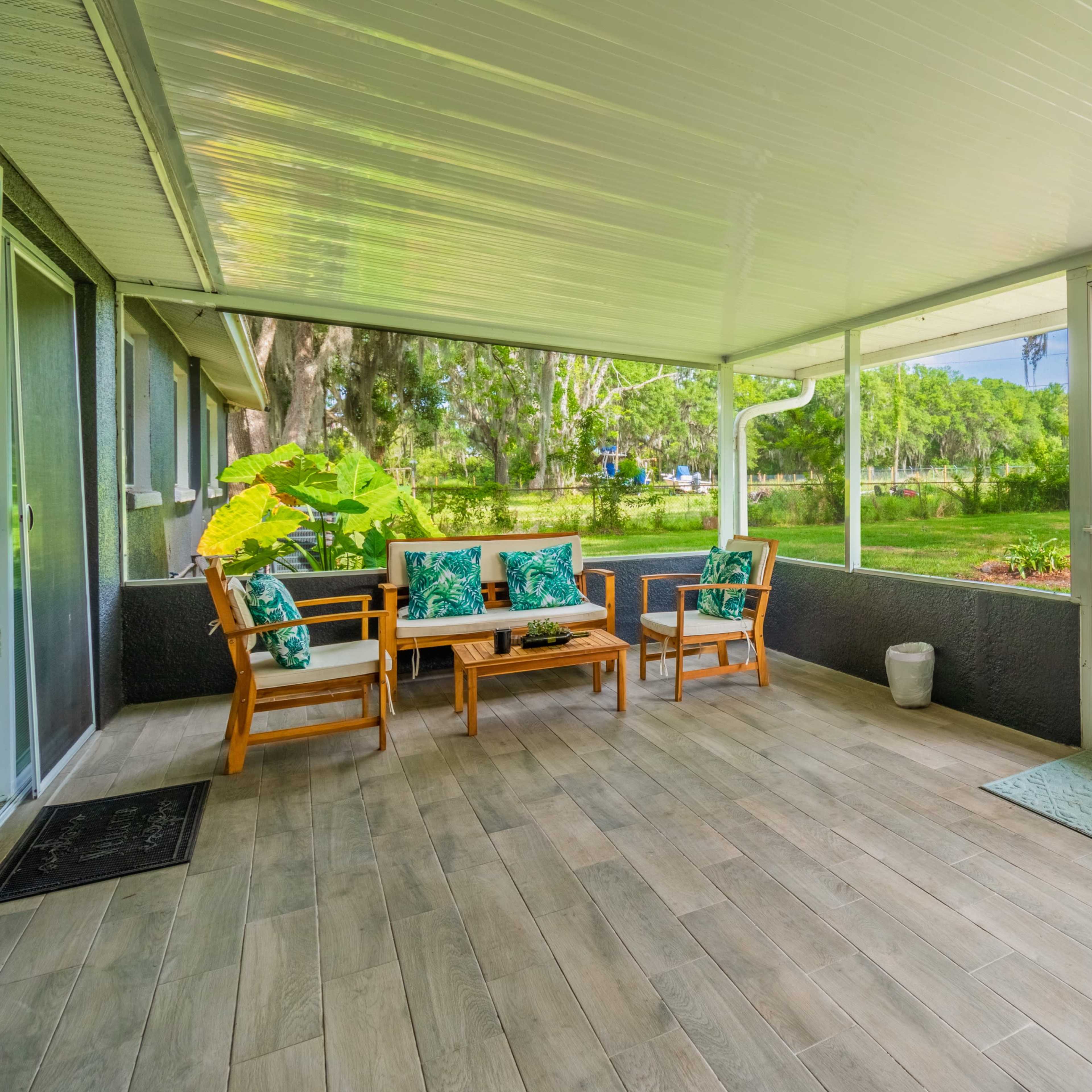 A covered porch with wooden furniture and a view of a green lawn surrounded by trees.
