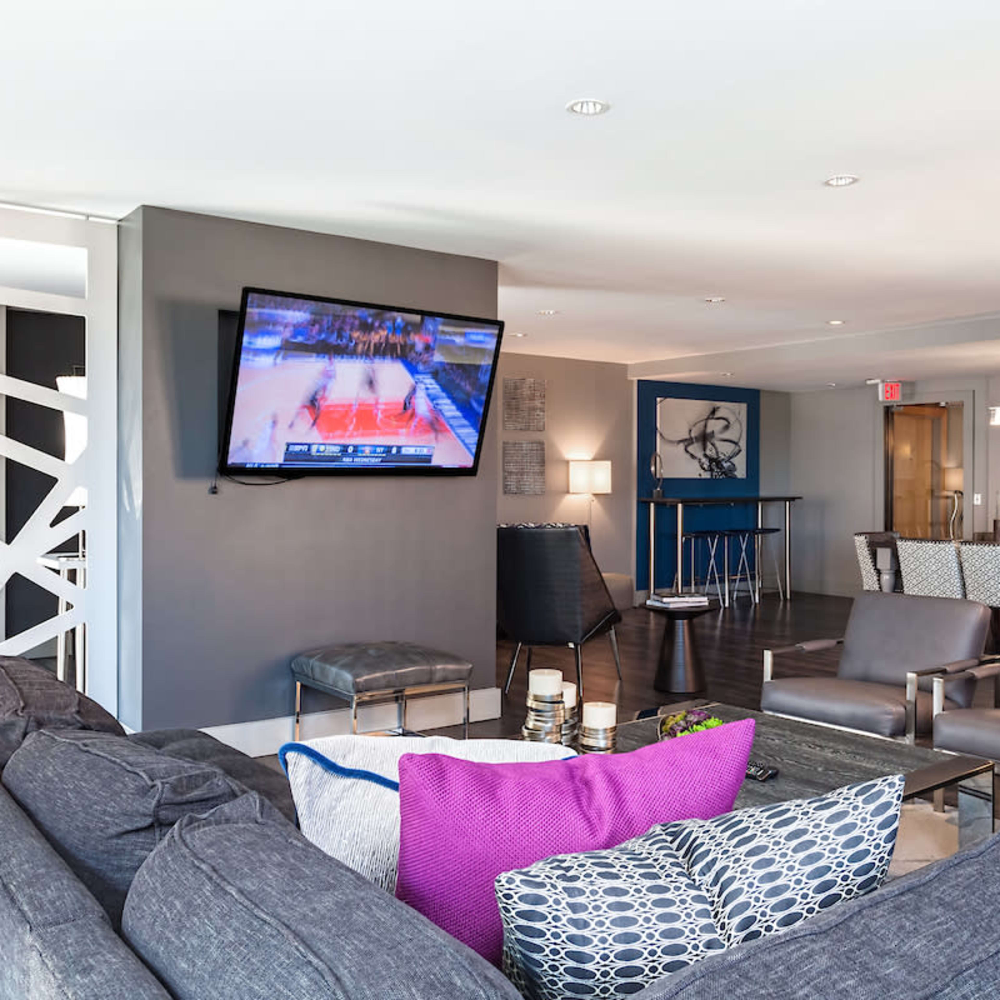 A modern lounge area with a large television displaying a basketball game, surrounded by comfortable seating and decorative elements.