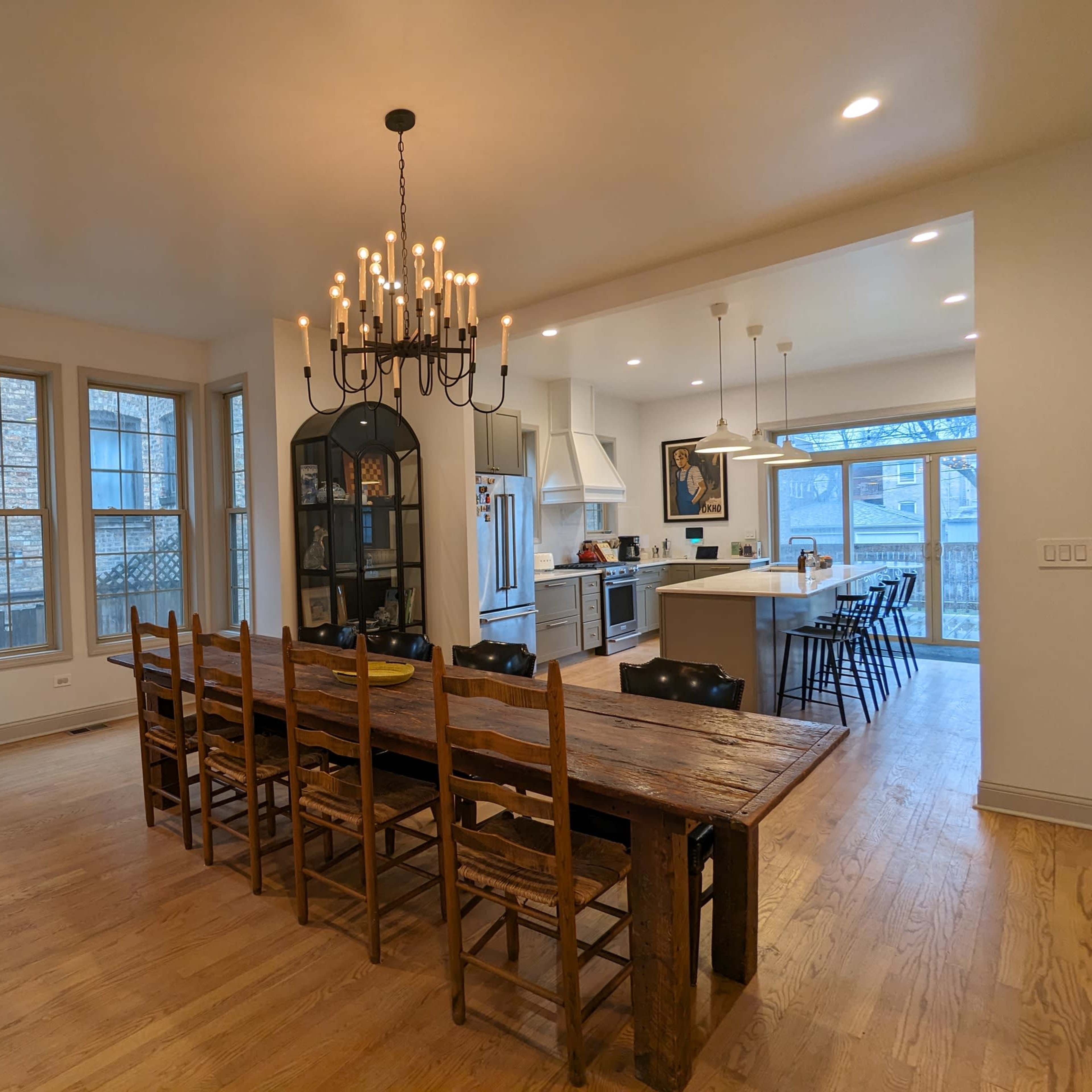 A spacious dining area with a long wooden table surrounded by eight chairs, leading into a modern kitchen with a large island and a chandelier overhead.