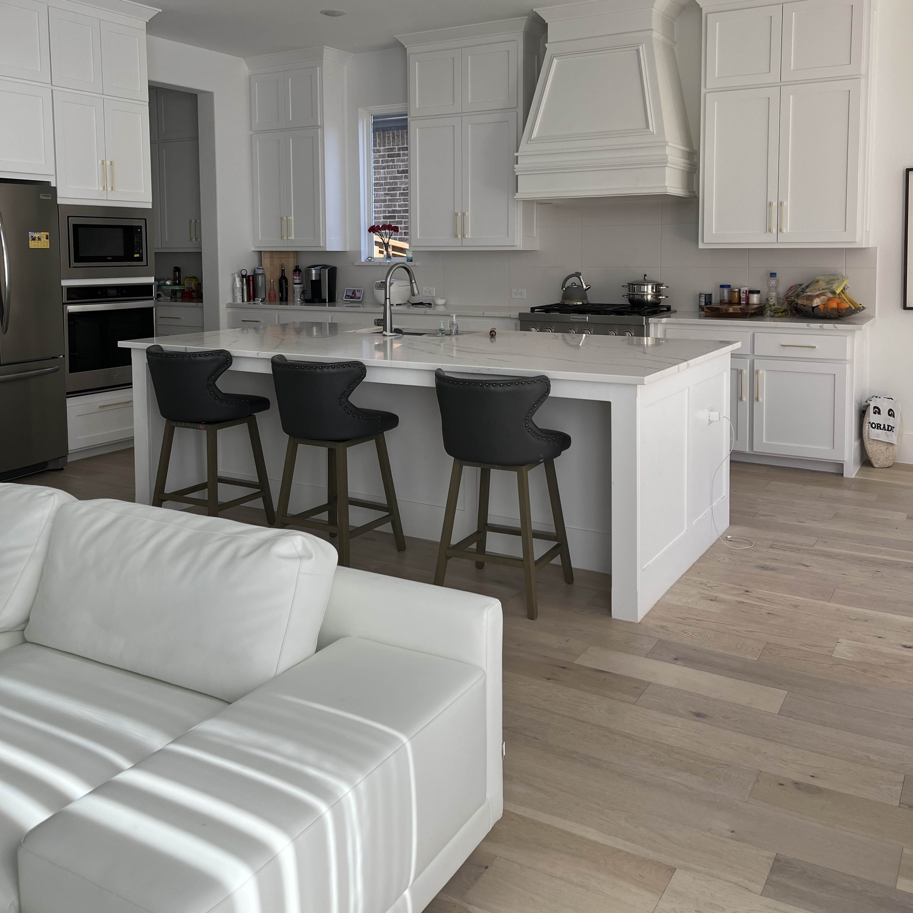 A modern kitchen with white cabinetry, a large island with four bar stools, and stainless steel appliances.