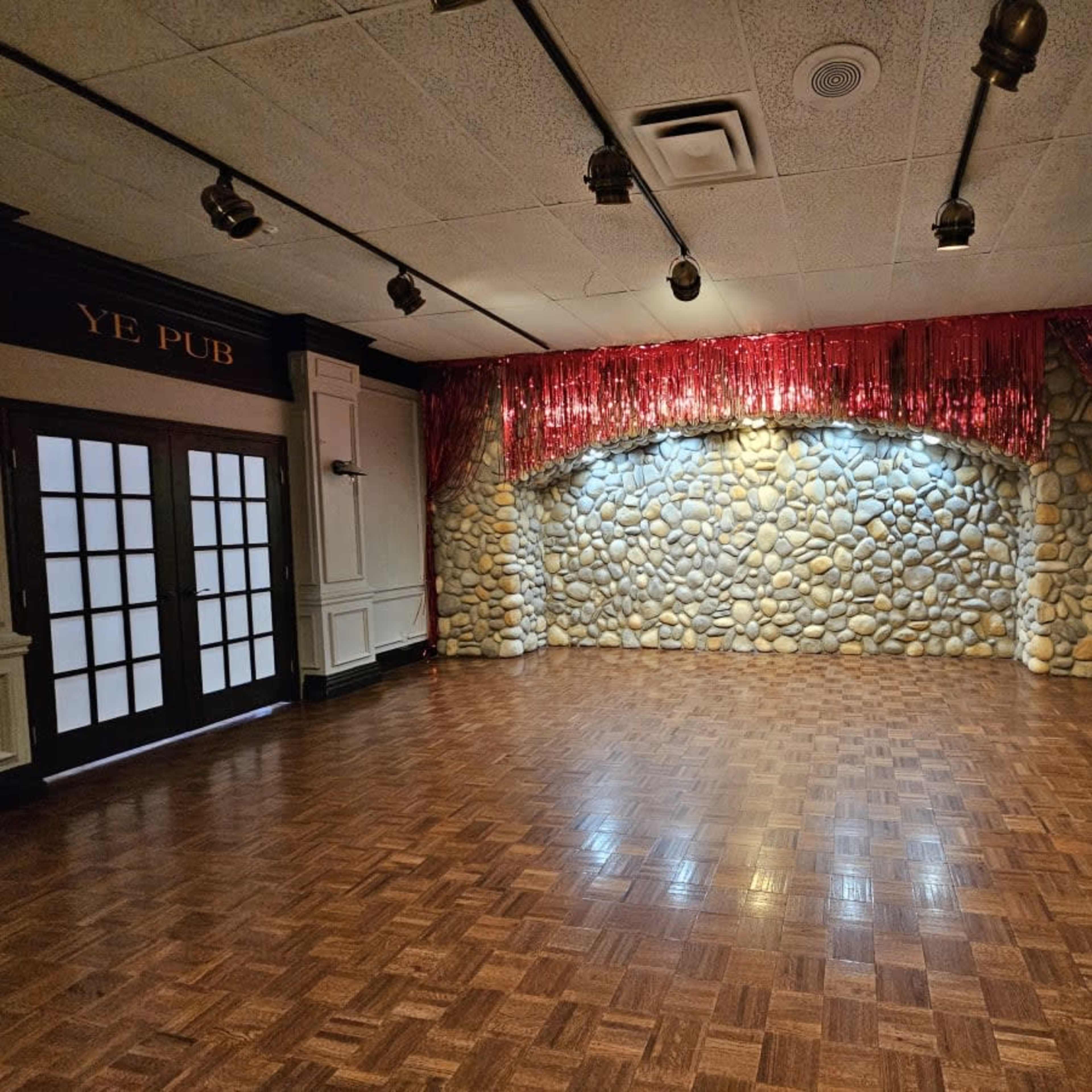 An empty room with a wooden floor, a stone wall backdrop, and red curtains, designed for events.