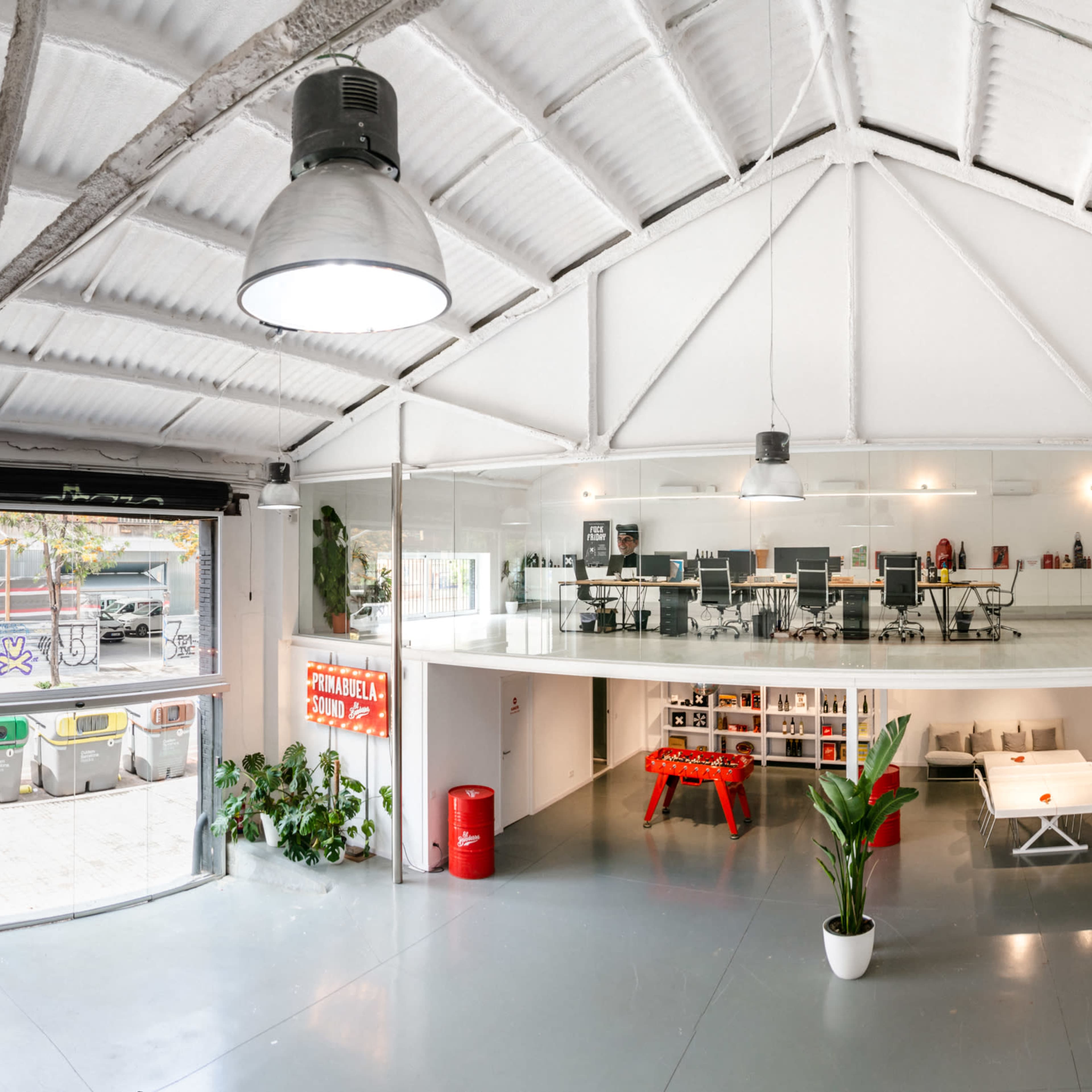 A modern open office space with a high ceiling, featuring a loft area above workstations and a communal area, along with a bar and seating arrangement on the lower level.