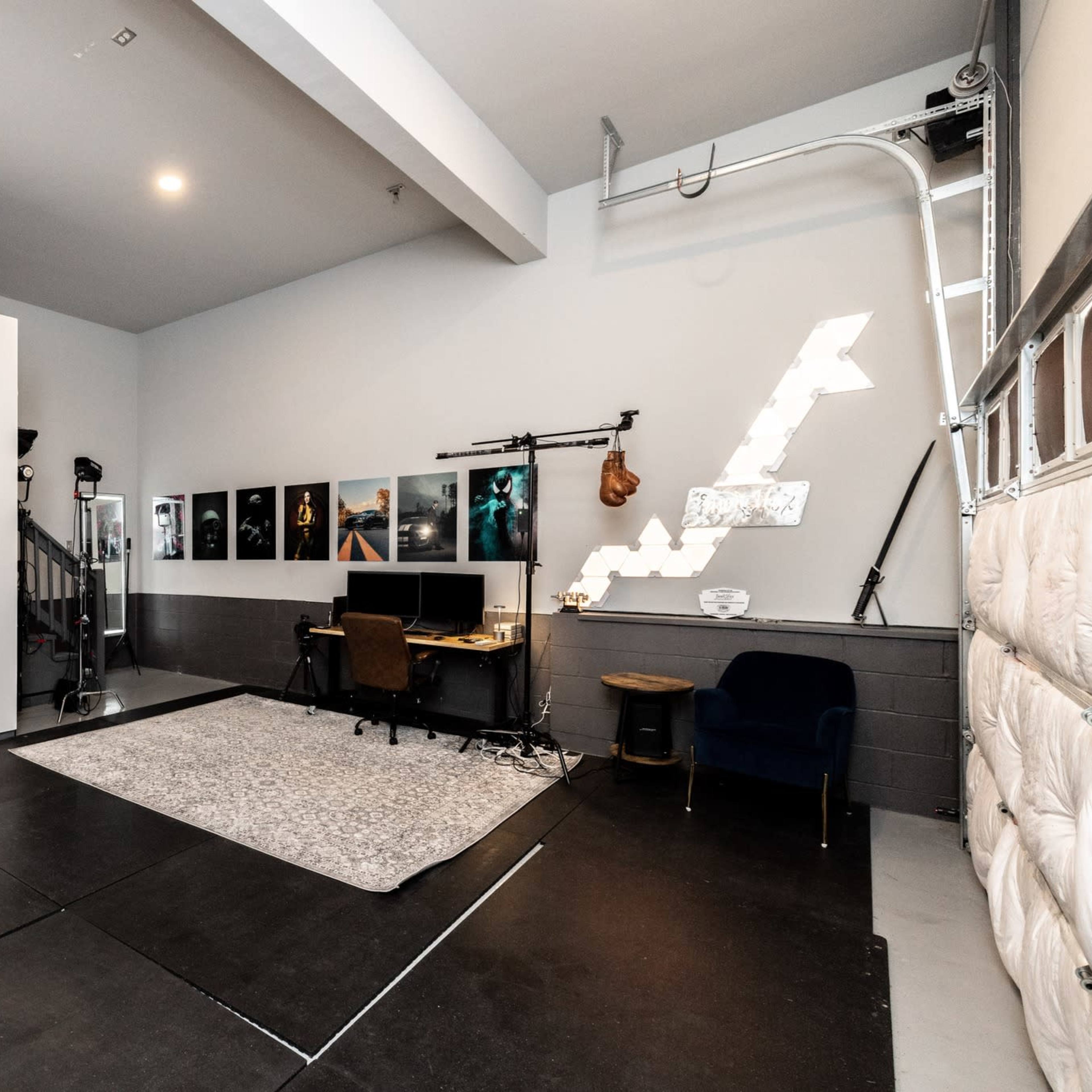 A spacious studio with a large white backdrop, a desk with a computer, and several framed pictures on the walls.