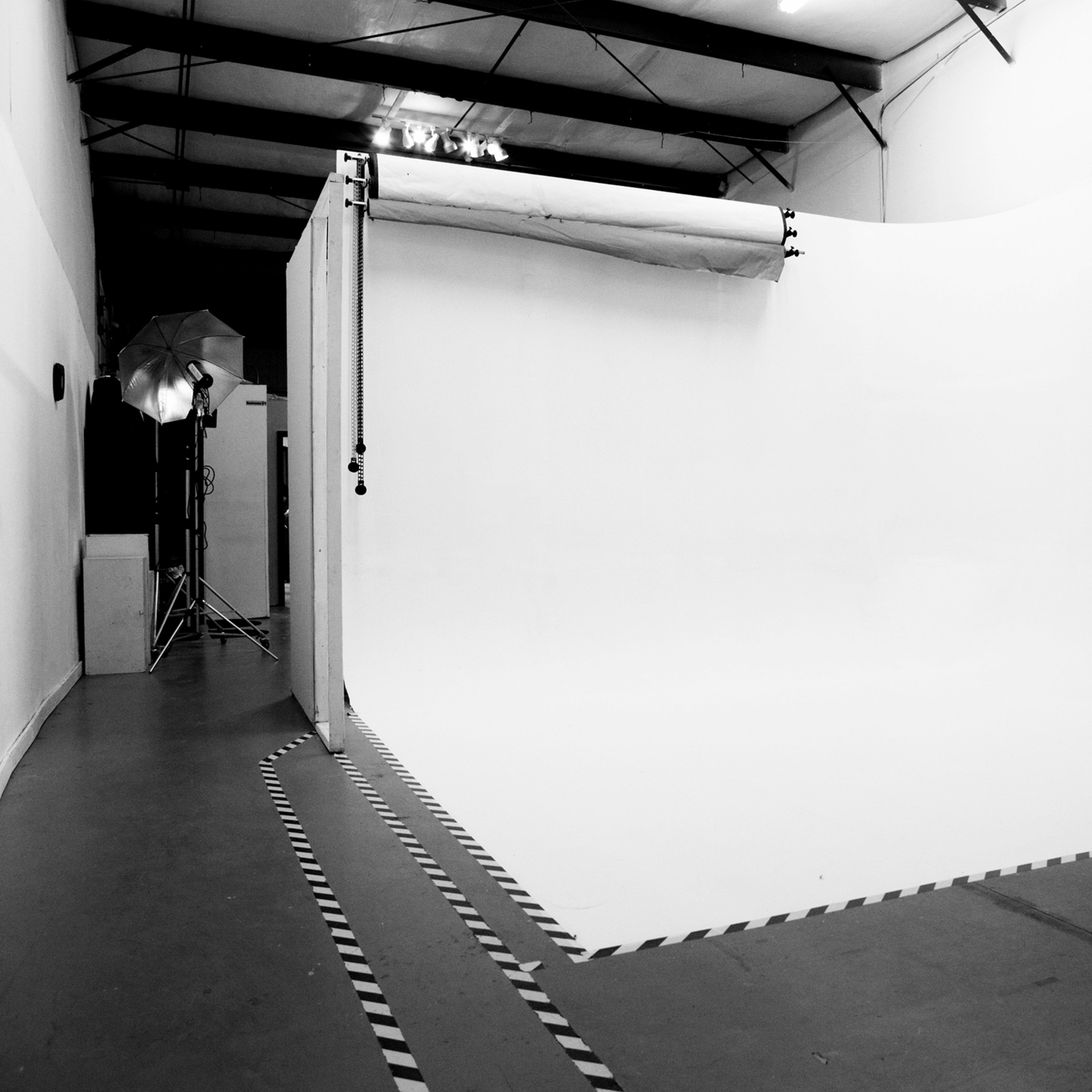 A photography studio with a large white backdrop and a smooth floor, illuminated by studio lights.