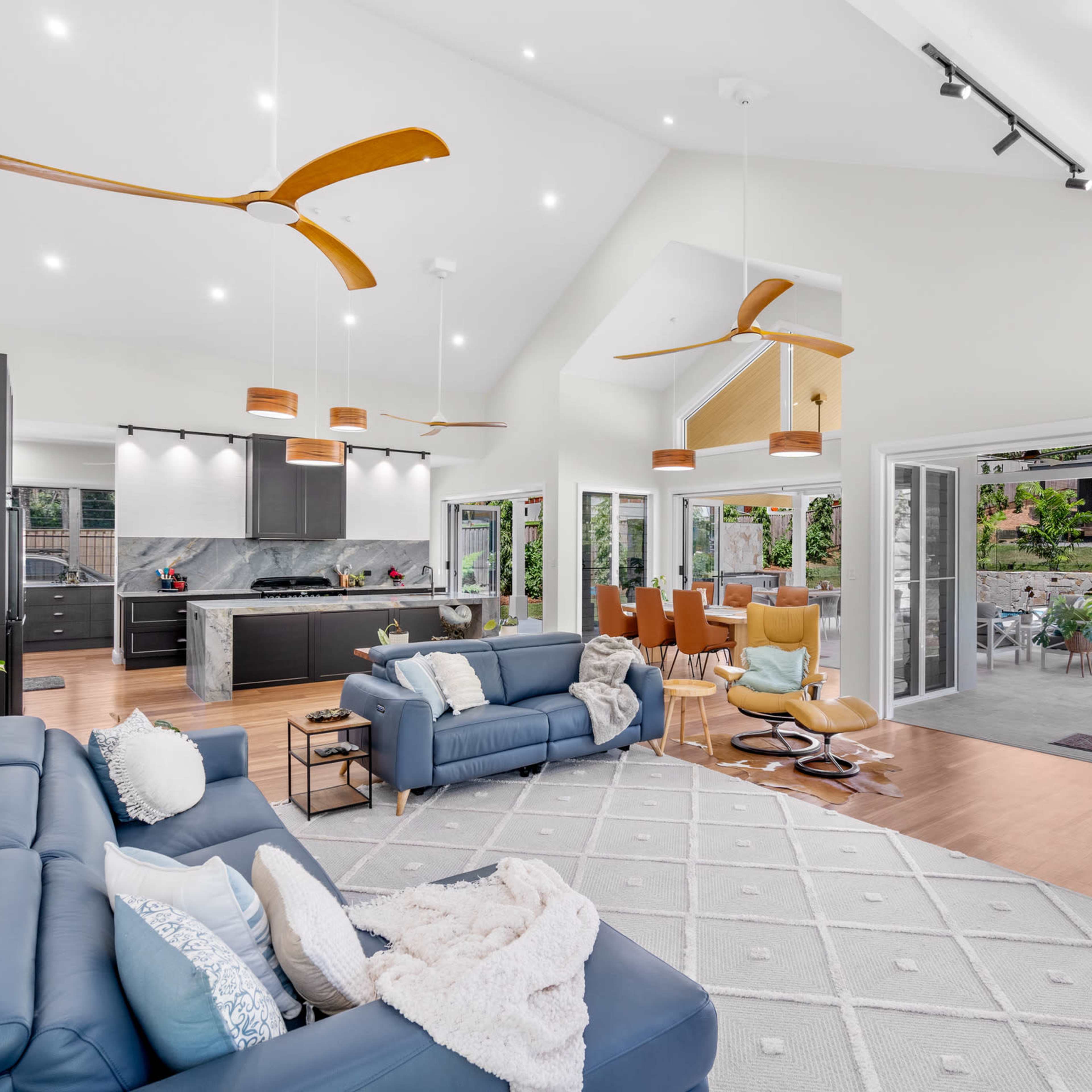 A modern open-concept living space with a living area, kitchen, and dining area, featuring large windows and a view of an outdoor patio with a pool.
