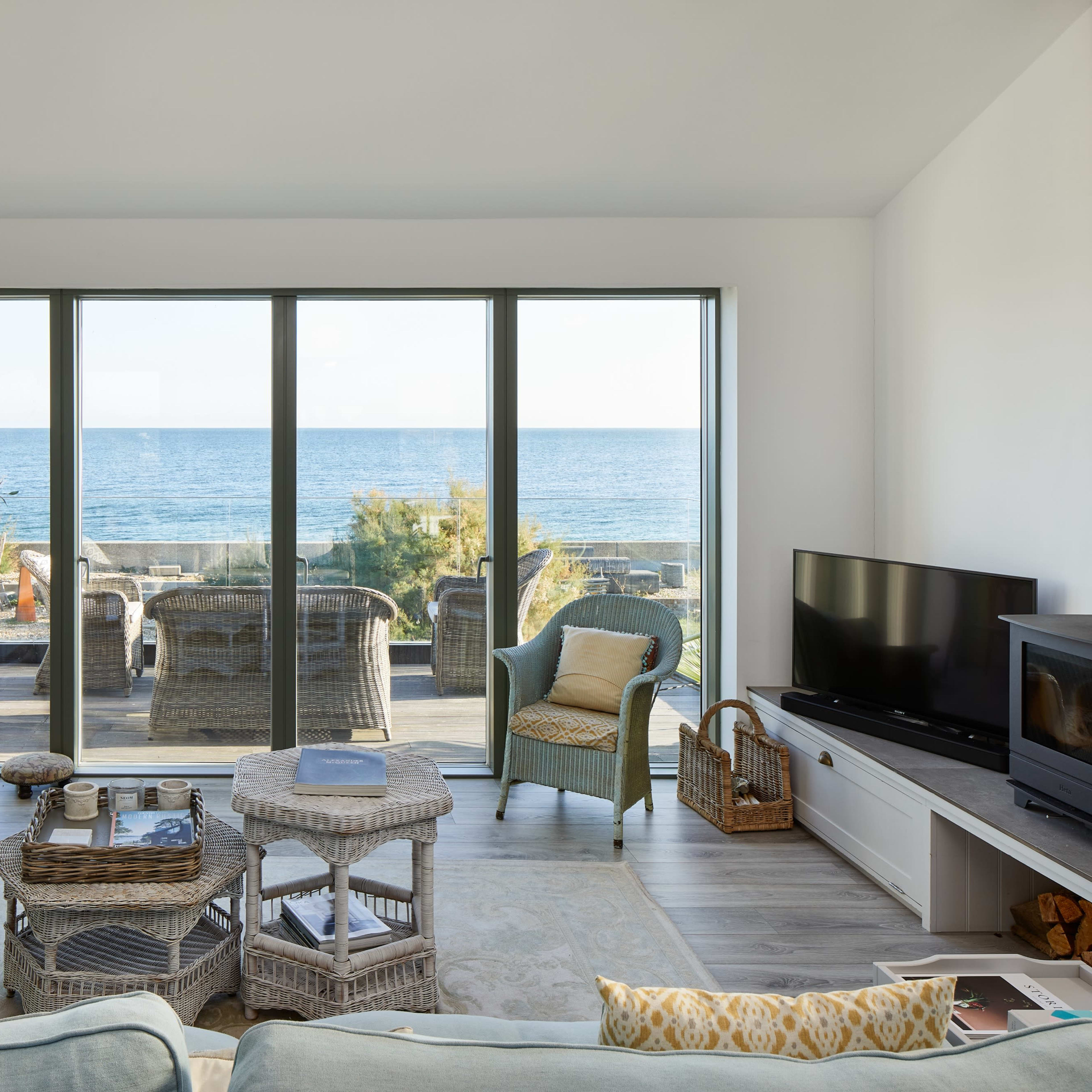 A modern living room features light-colored furniture and large glass doors that open to a view of the ocean.