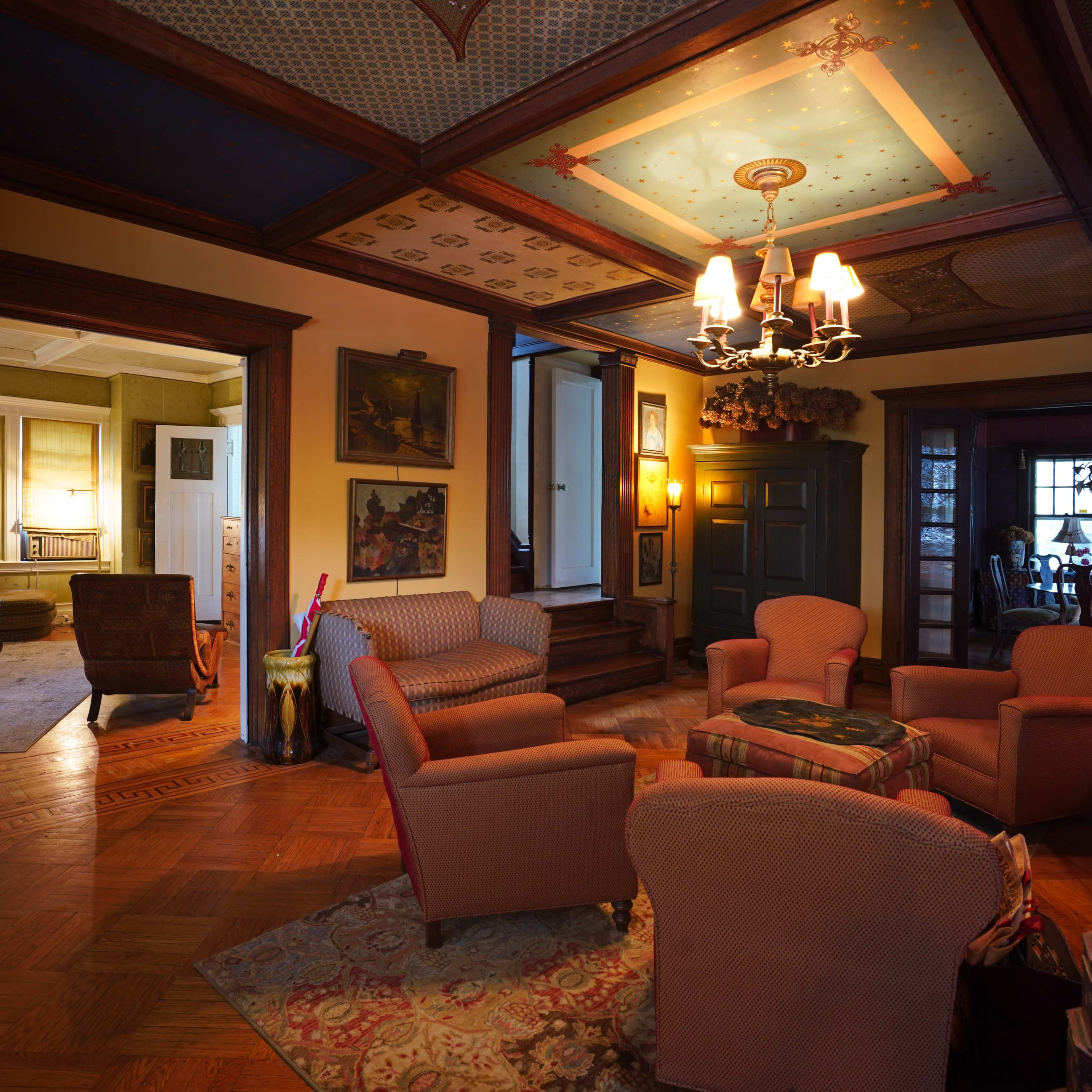 A spacious living room with four upholstered chairs arranged around a small table, featuring decorative ceilings and wooden accents, leading to another room visible in the background.