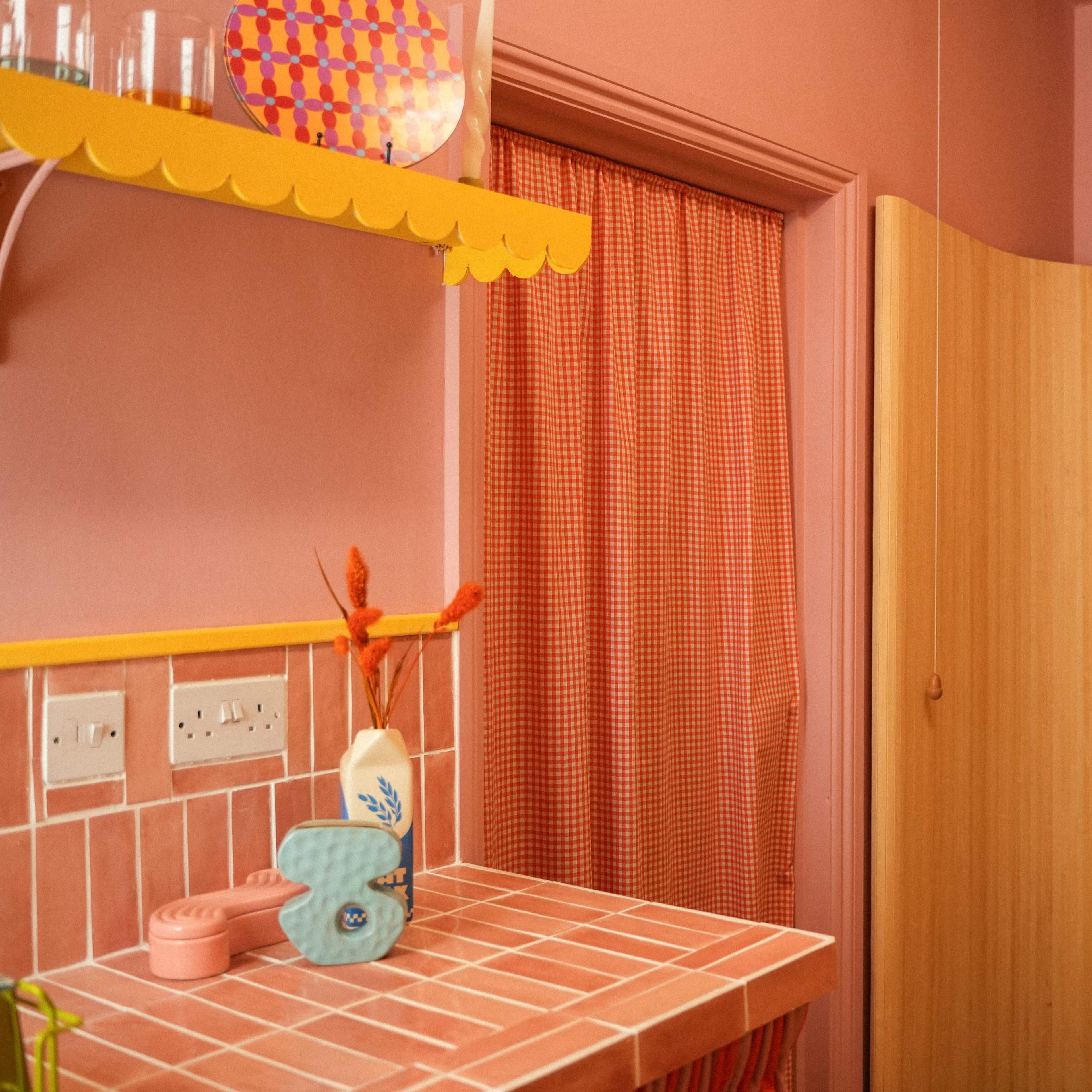 A brightly colored kitchen corner featuring pink walls, a tiled countertop, and a doorway draped with a yellow curtain.