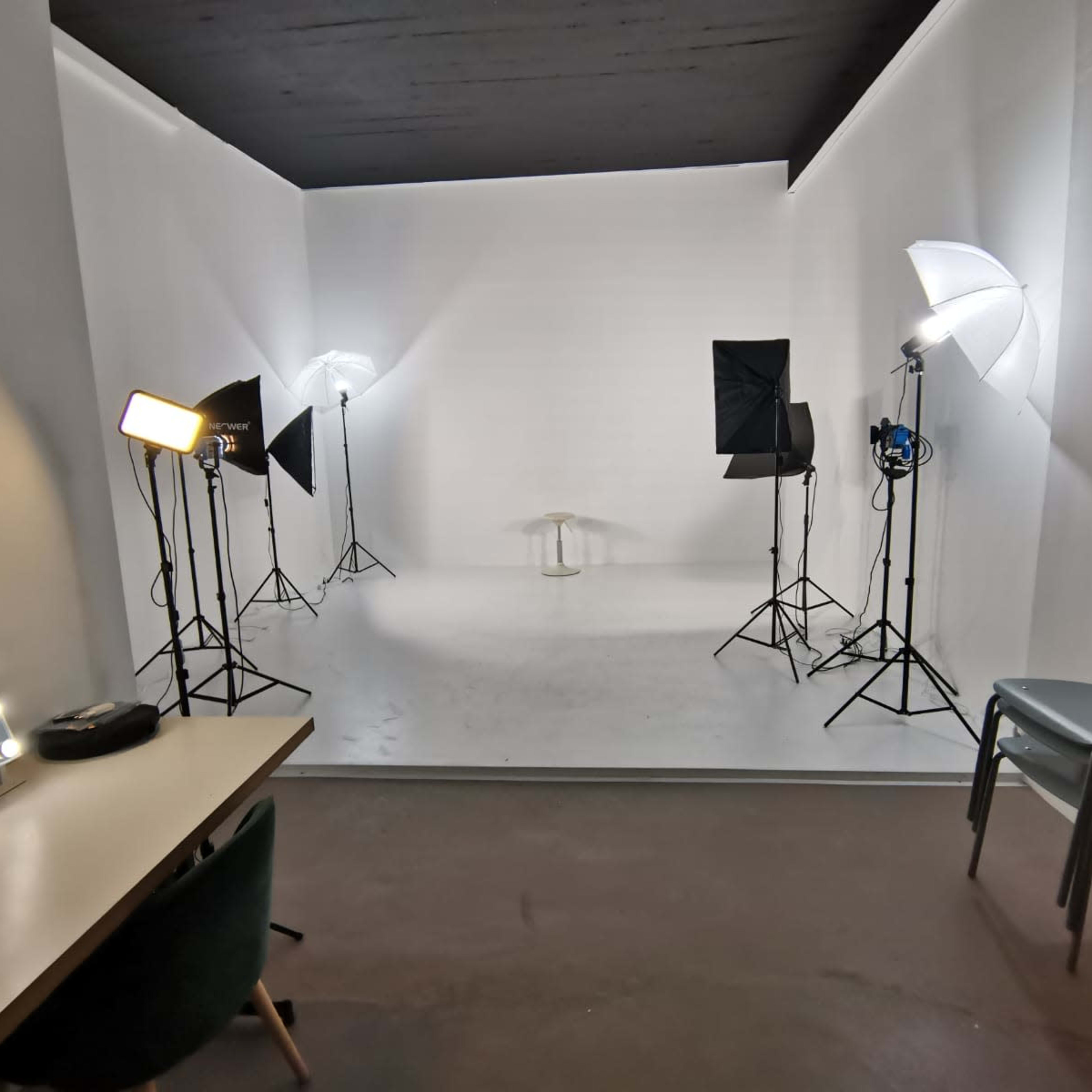 A blank white studio space equipped with lighting setup and a mirrored vanity table in the foreground.