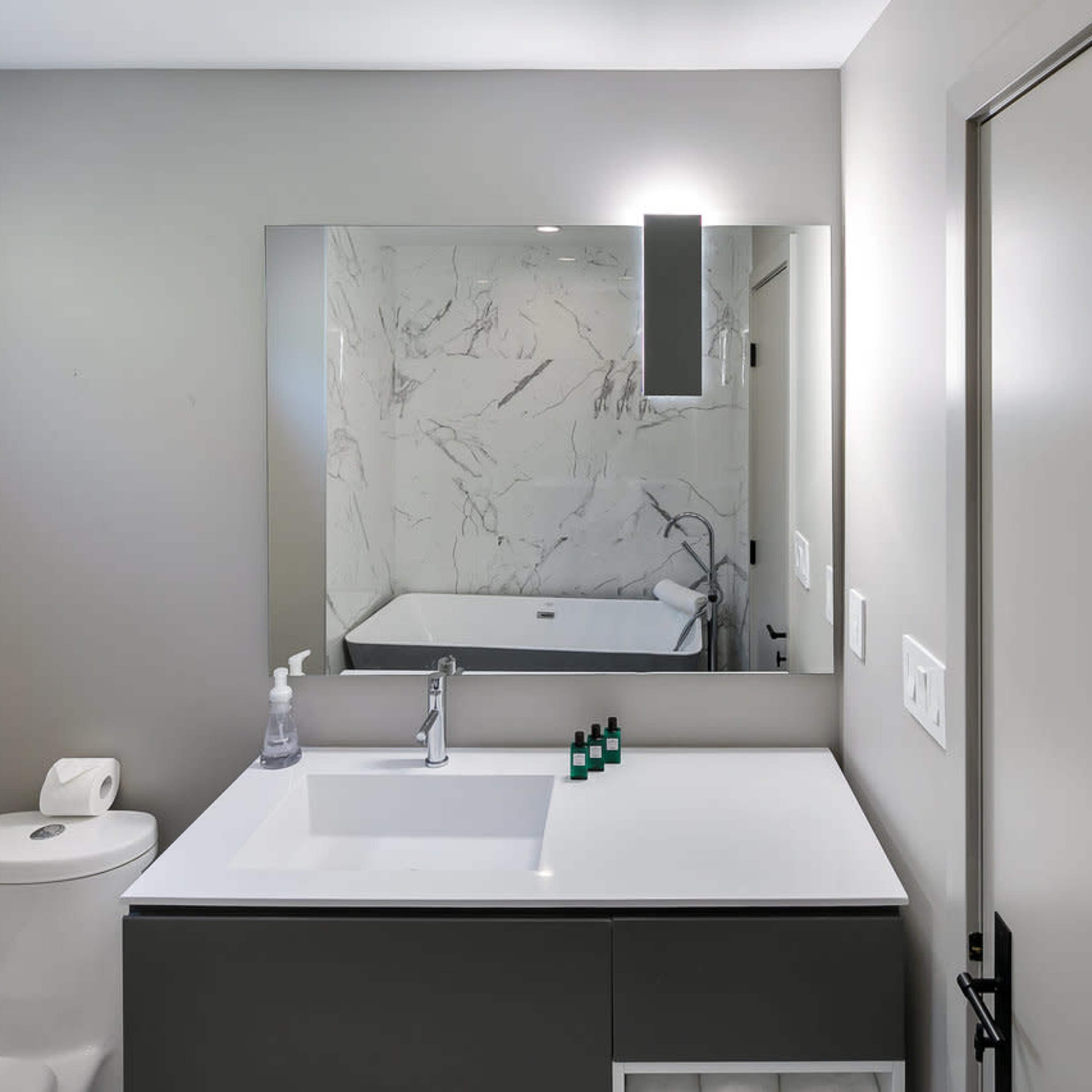 A modern bathroom features a white countertop sink, a wall-mounted mirror, a stylish light fixture, and a toilet against a gray wall with marble accents.