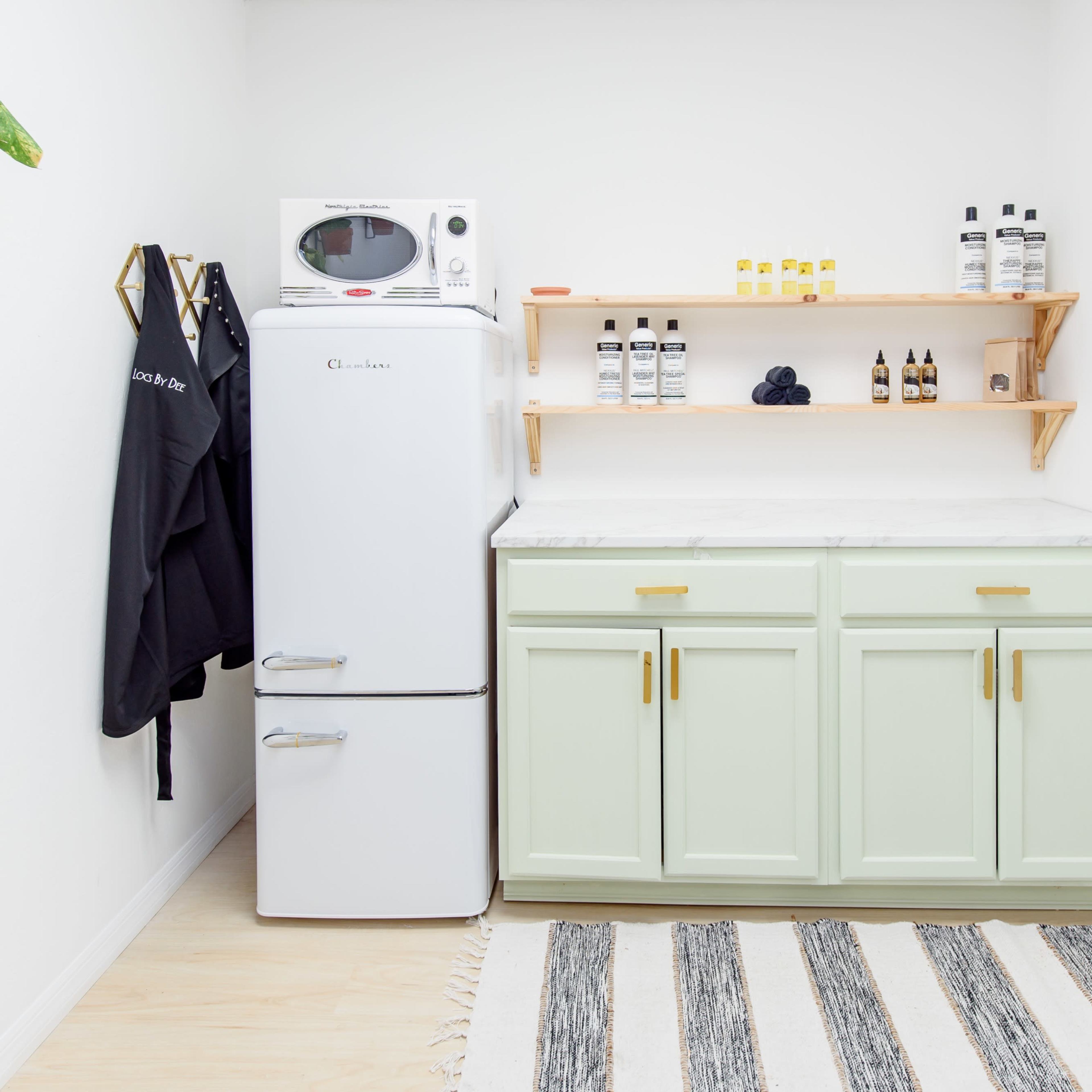 A kitchen corner with a white refrigerator, a microwave, a marble countertop, green cabinets, and a shelf holding various bottles.