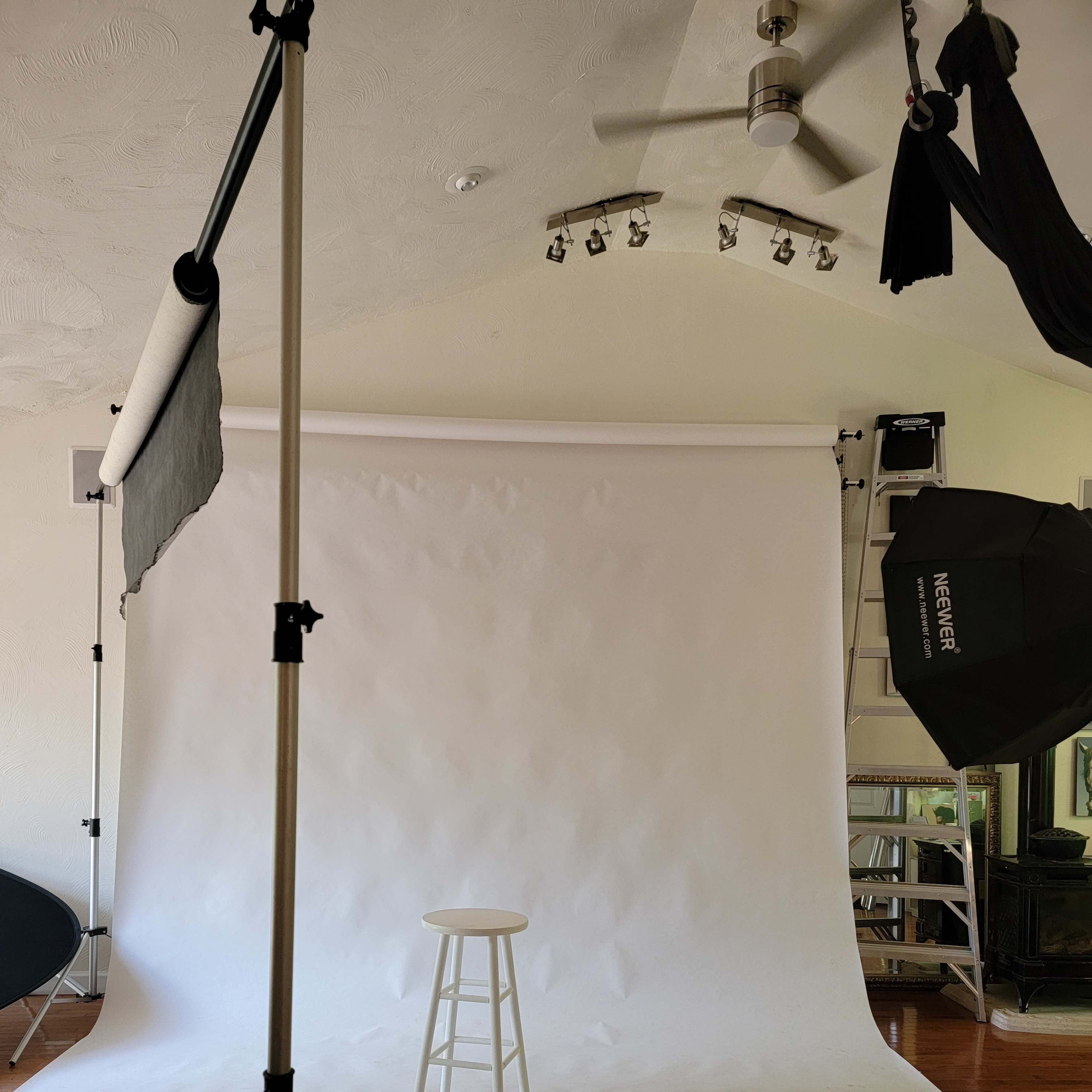 An empty photography studio with a white backdrop and a single stool positioned in front of it.