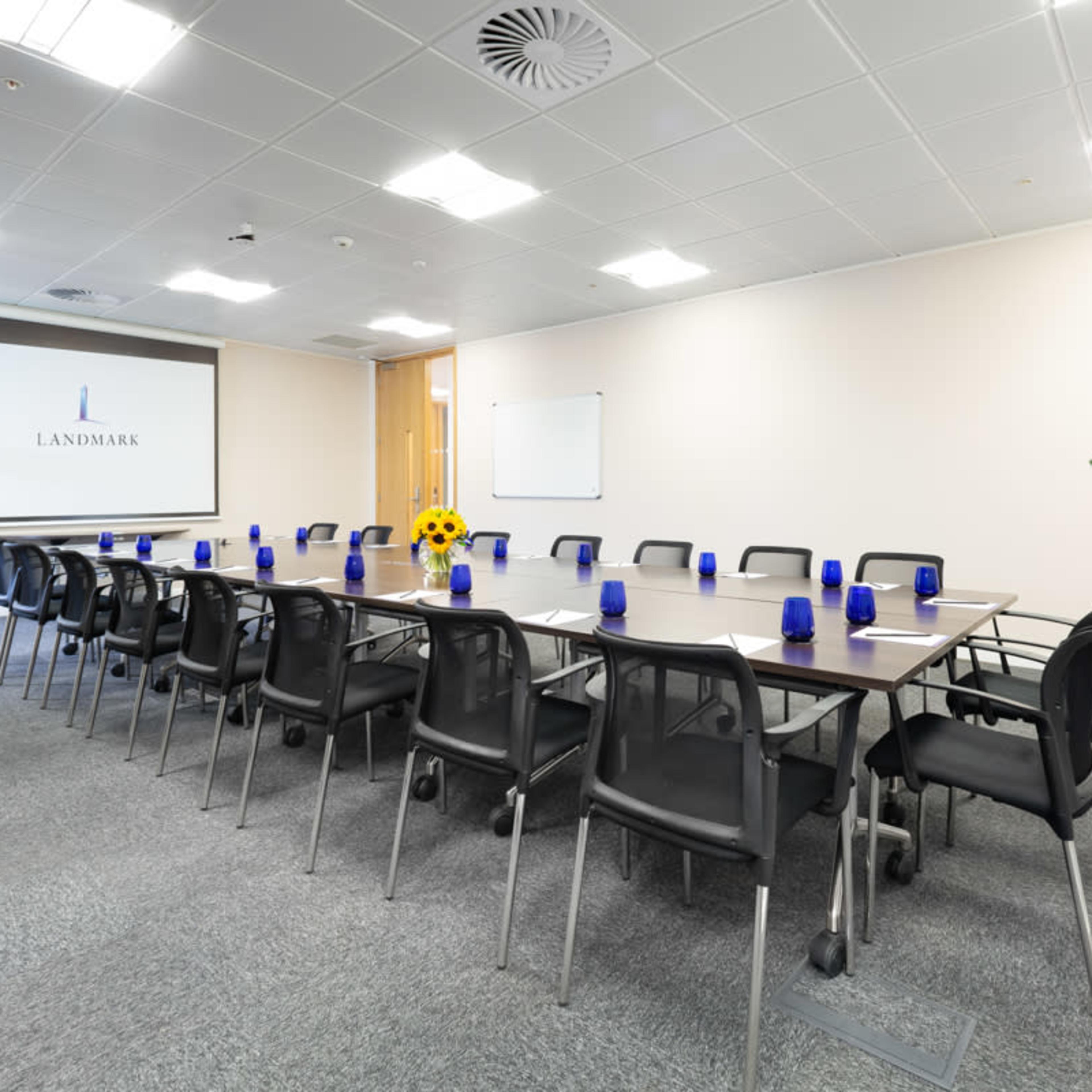 A modern conference room with a long table surrounded by black chairs, blue vases on the table, and a large screen displaying the word "LANDMARK."
